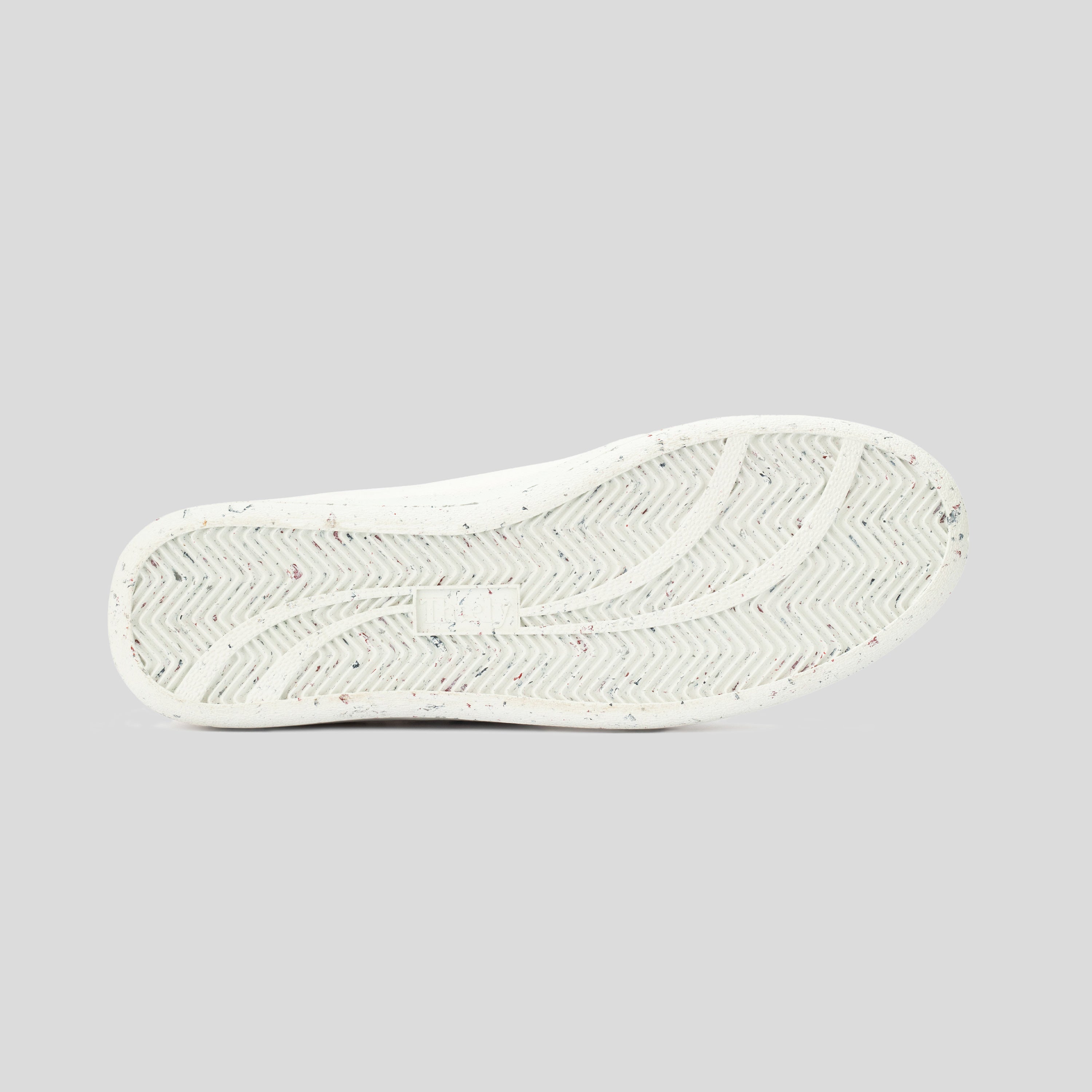 White sneaker outsole with herringbone tread pattern and multicolor speckles on light background