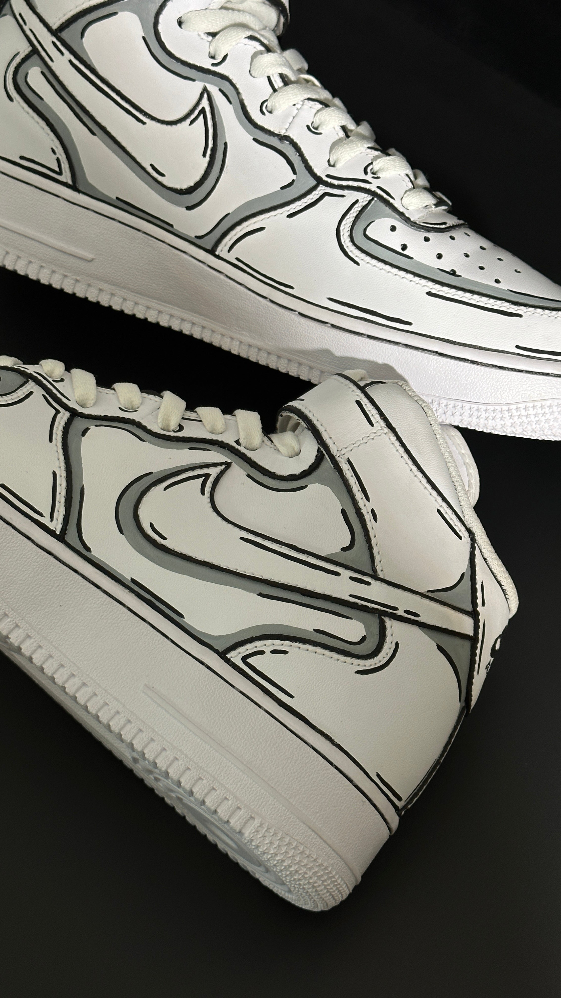 White streetwear sneakers with bold black graphic outlines on a black background