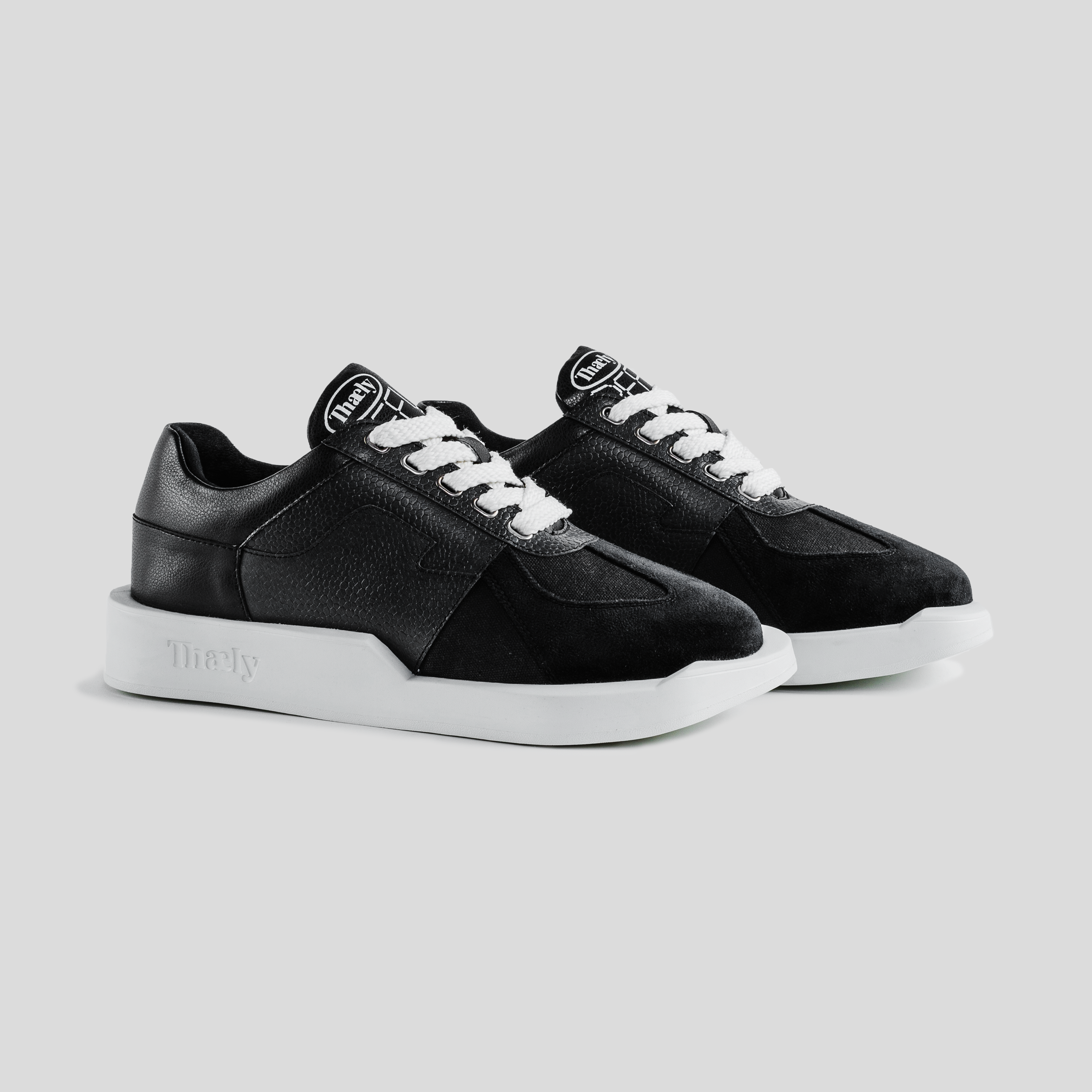 Black low-top streetwear sneakers with white soles and laces on a grey background.