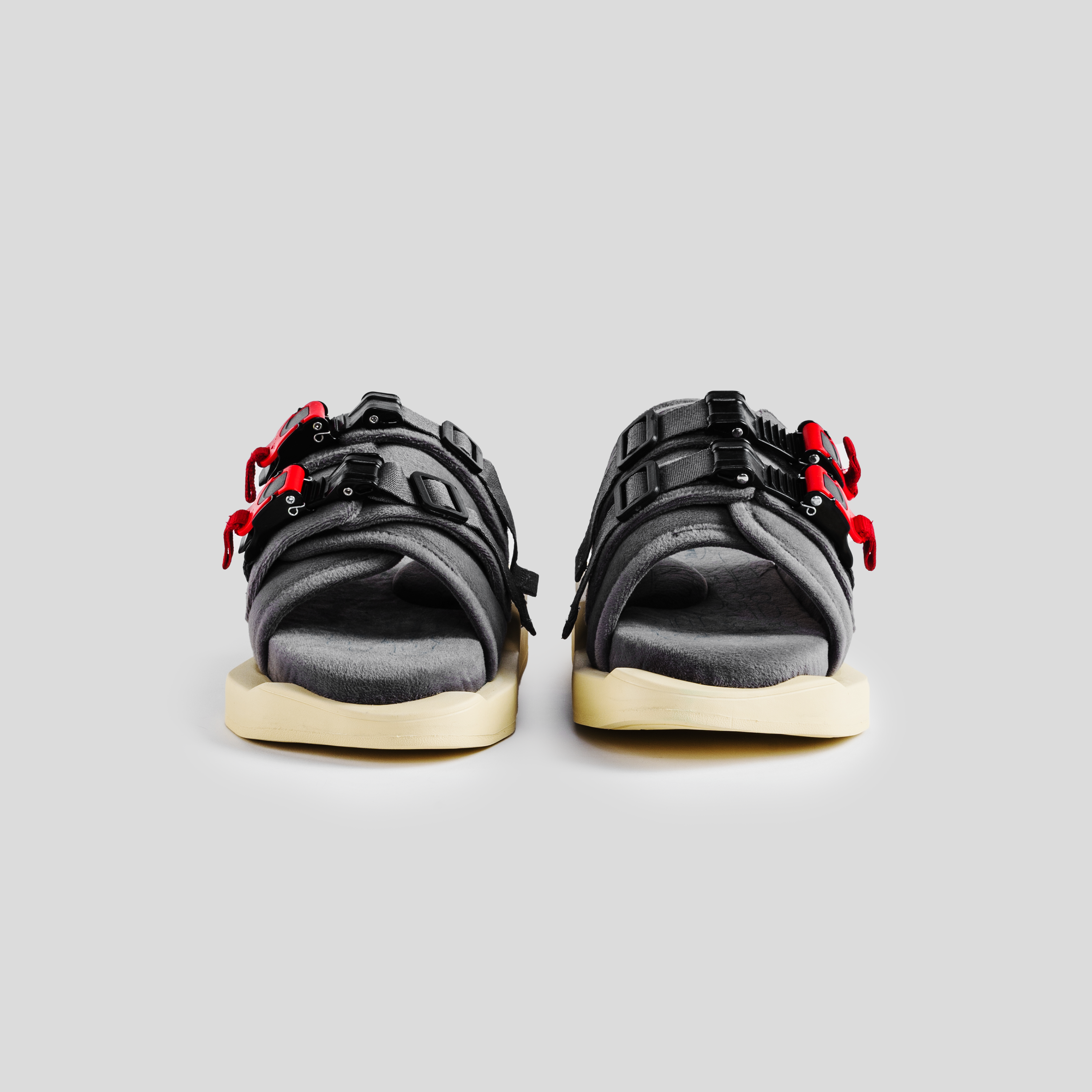 Front view of gray streetwear sandals with black and red buckles on thick cream soles