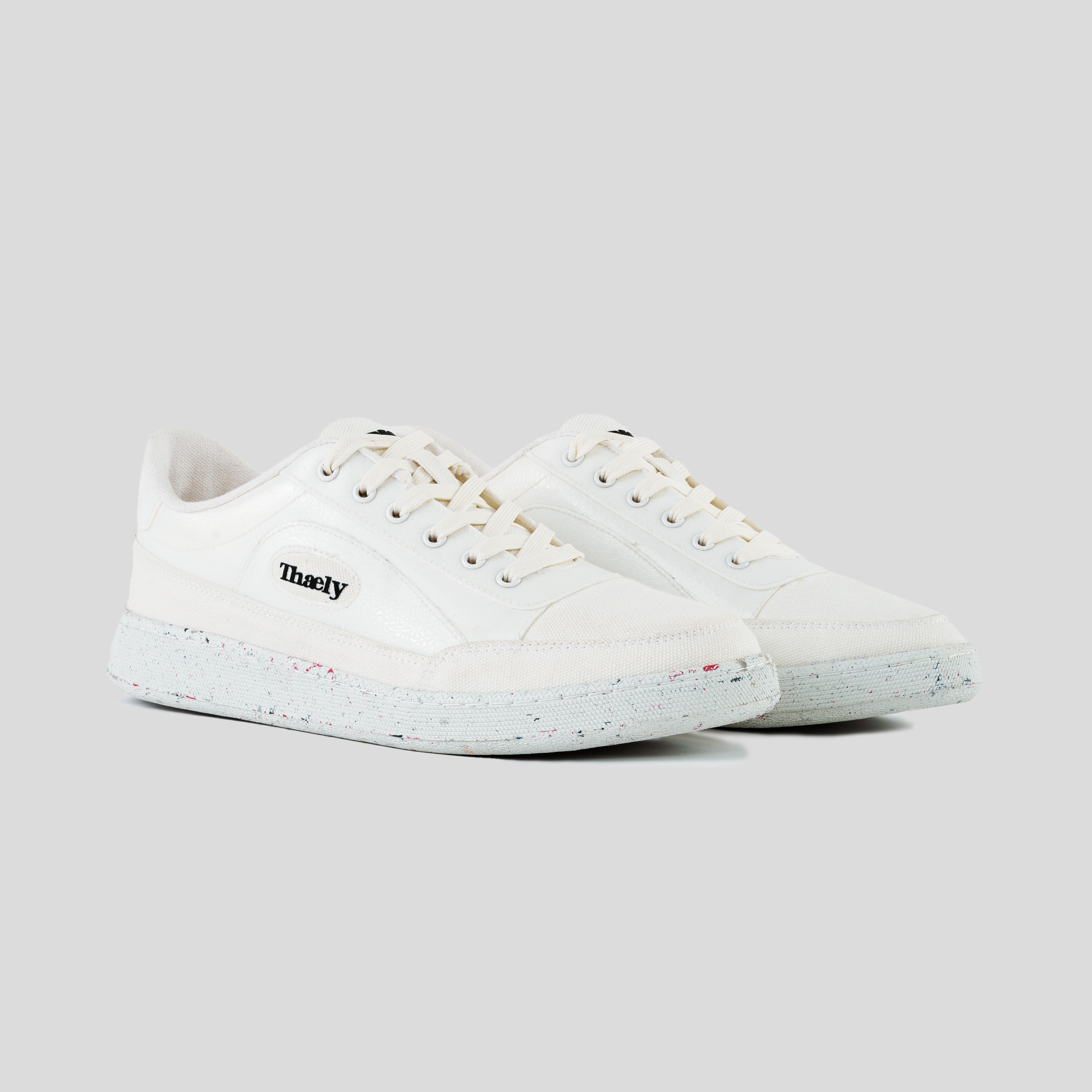 White low-top streetwear sneakers with speckled sole, lace-up front, and side logo text.