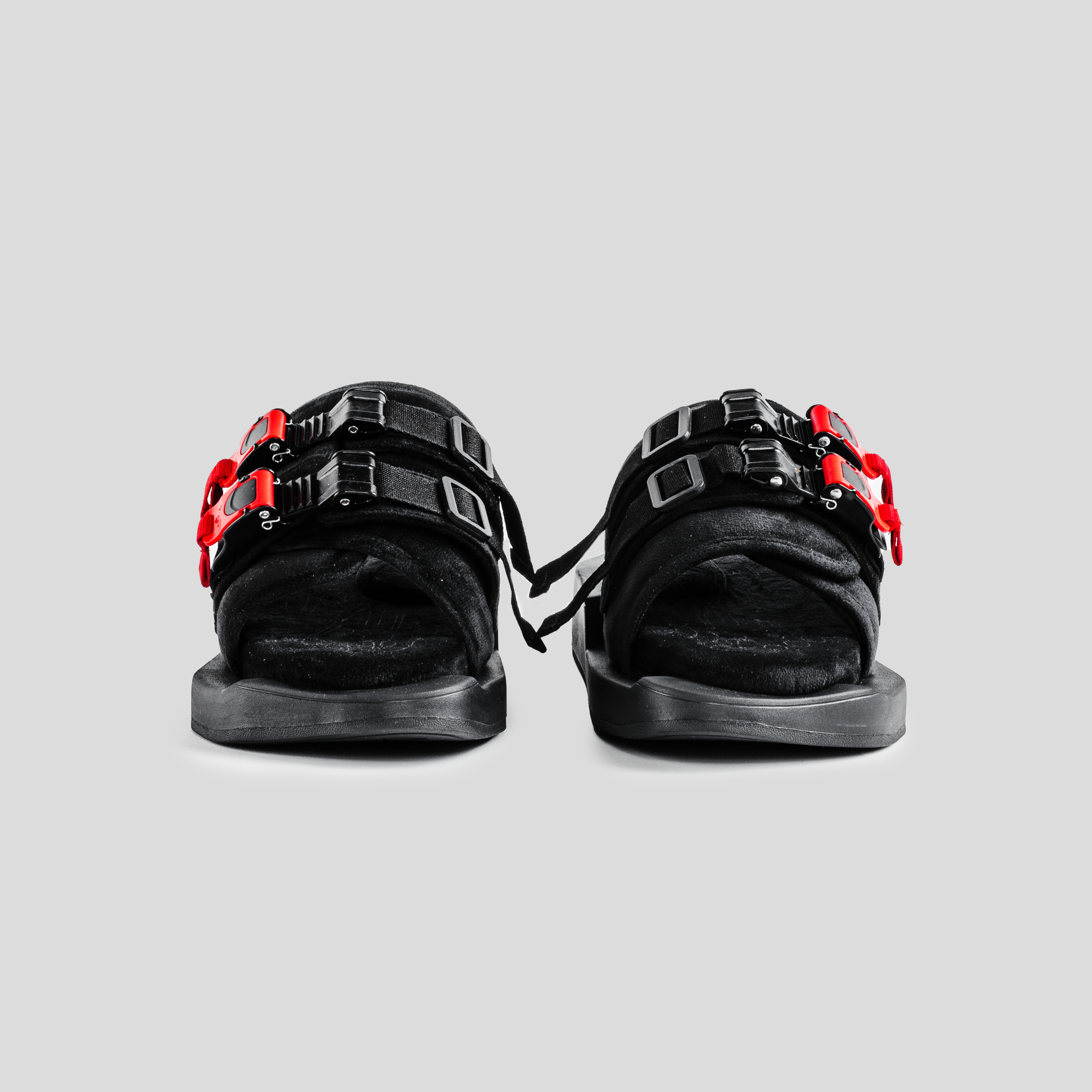 Black streetwear sandals with red and black buckle straps on a gray background