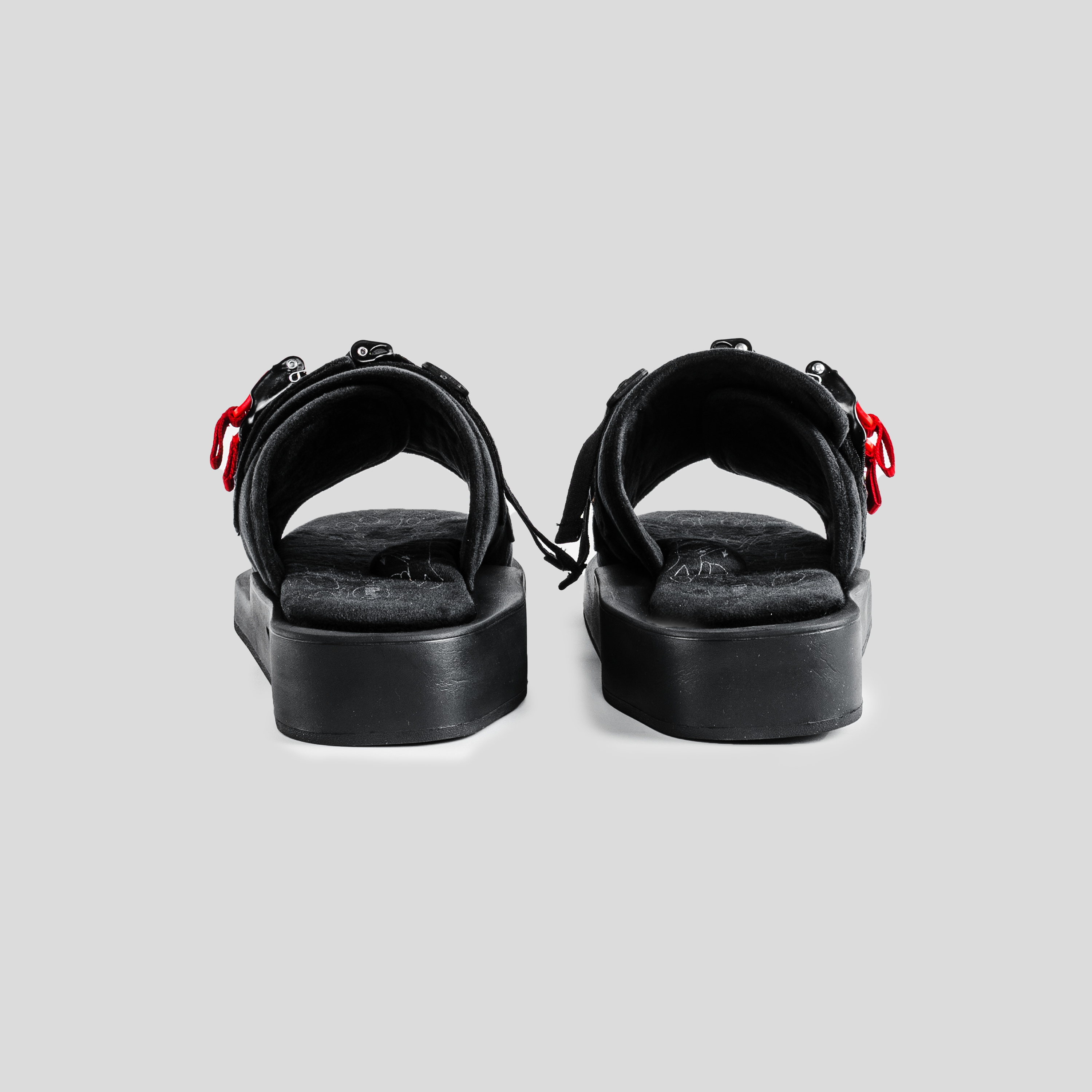 Rear view of black streetwear sandals with red accents and thick soles on grey background