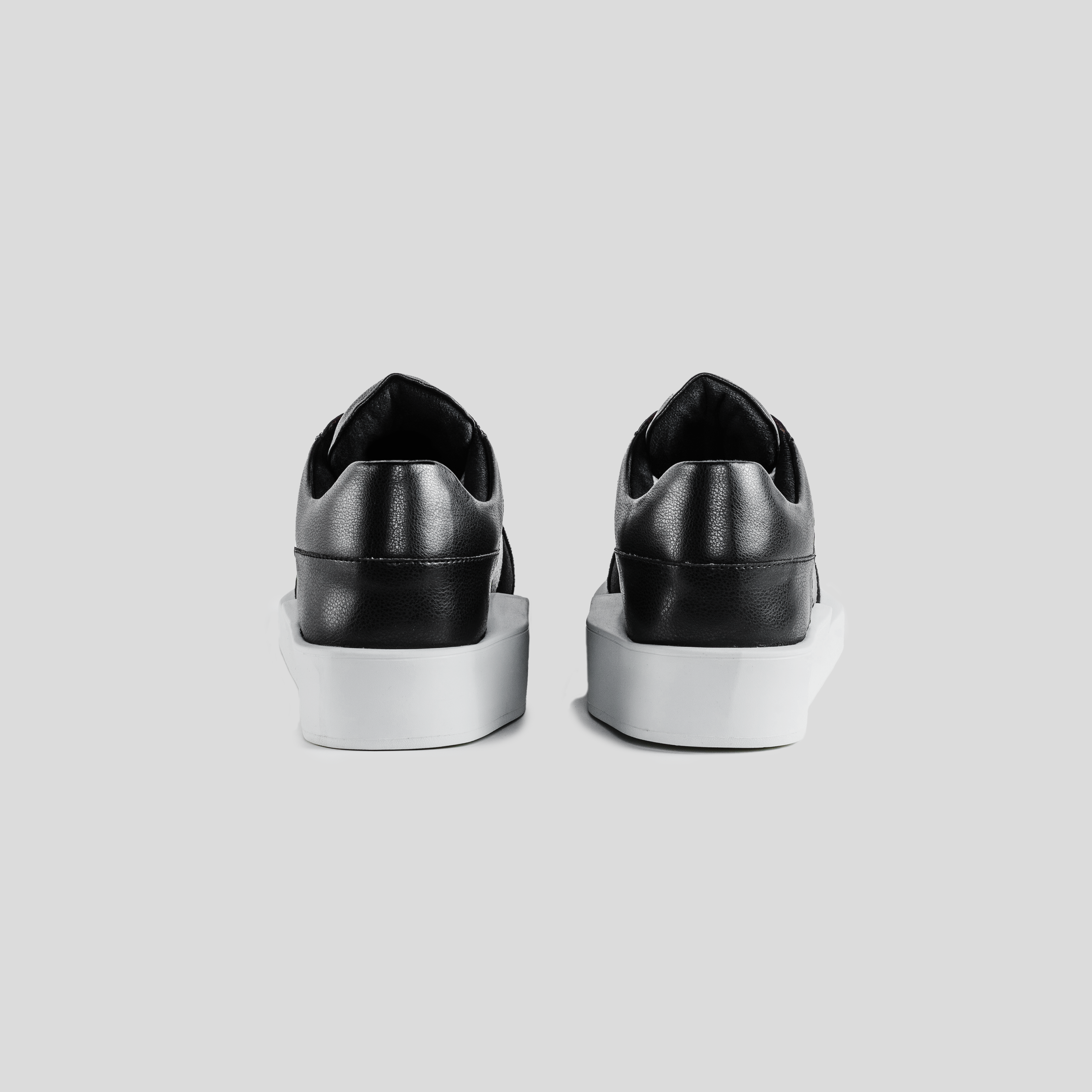 Back view of black leather low-top sneakers with white chunky soles on gray background
