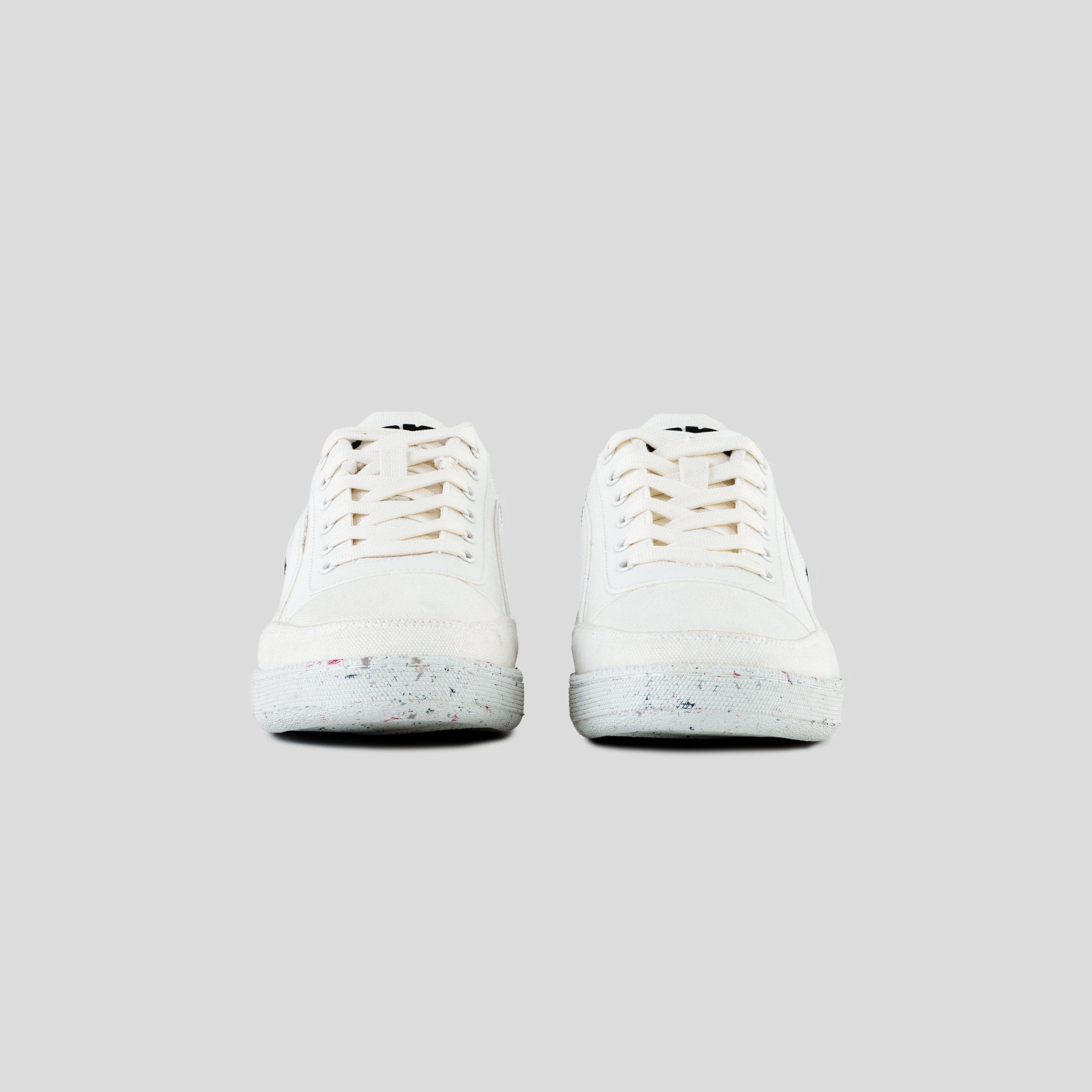 Front view of white low-top sneakers with speckled soles on a light gray background