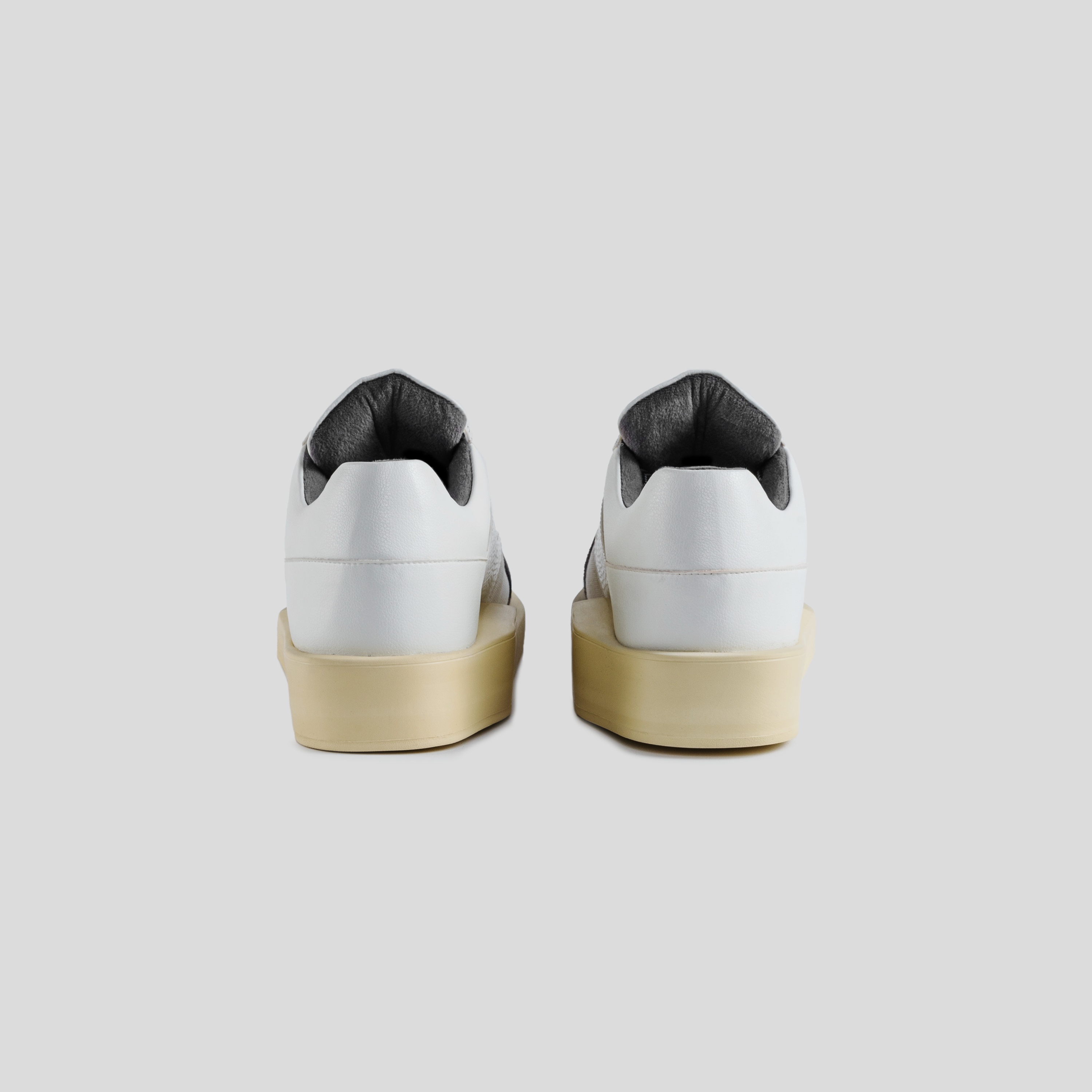 Back view of white leather streetwear sneakers with beige soles on a gray background