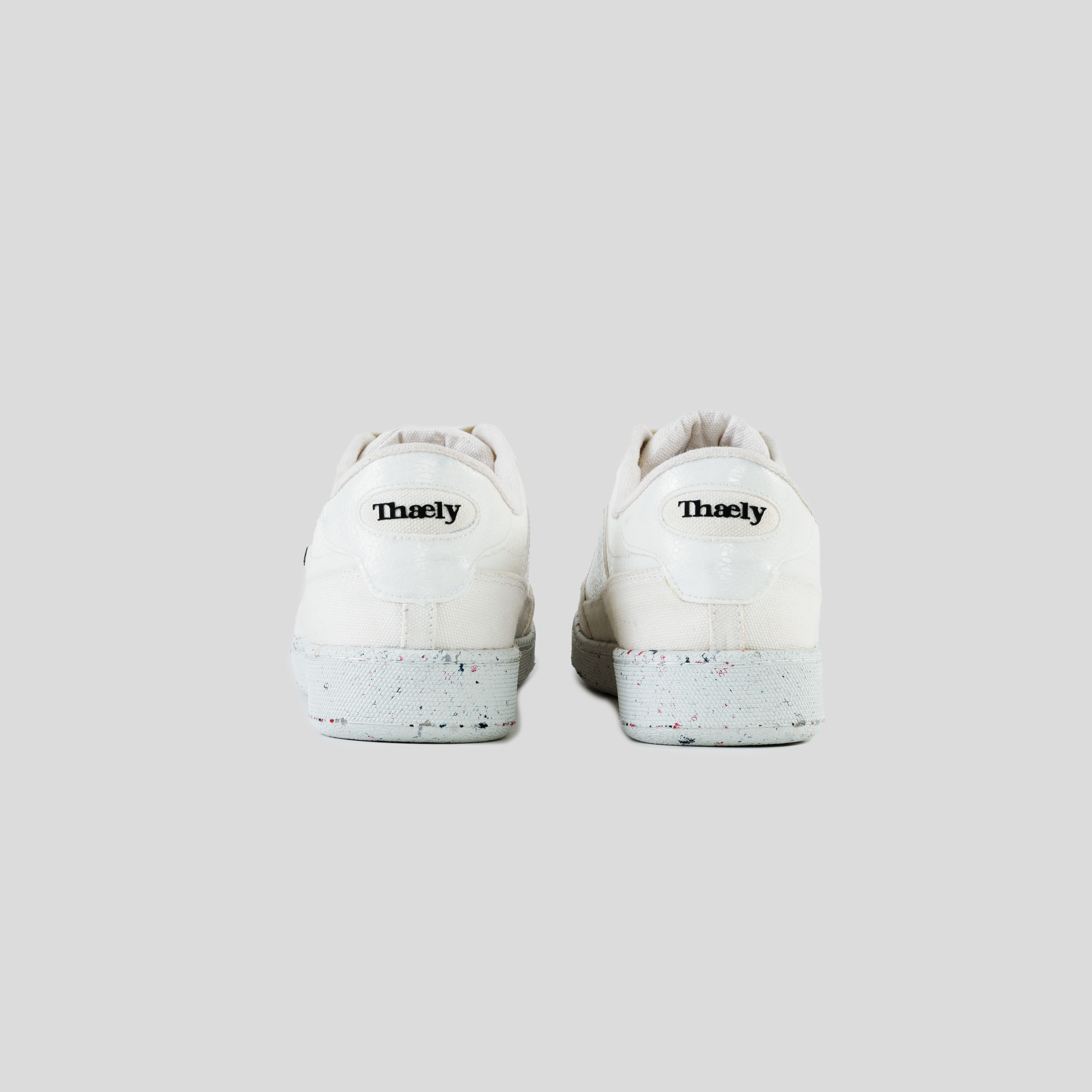 White streetwear sneakers with speckled soles, shown from the back on a neutral background