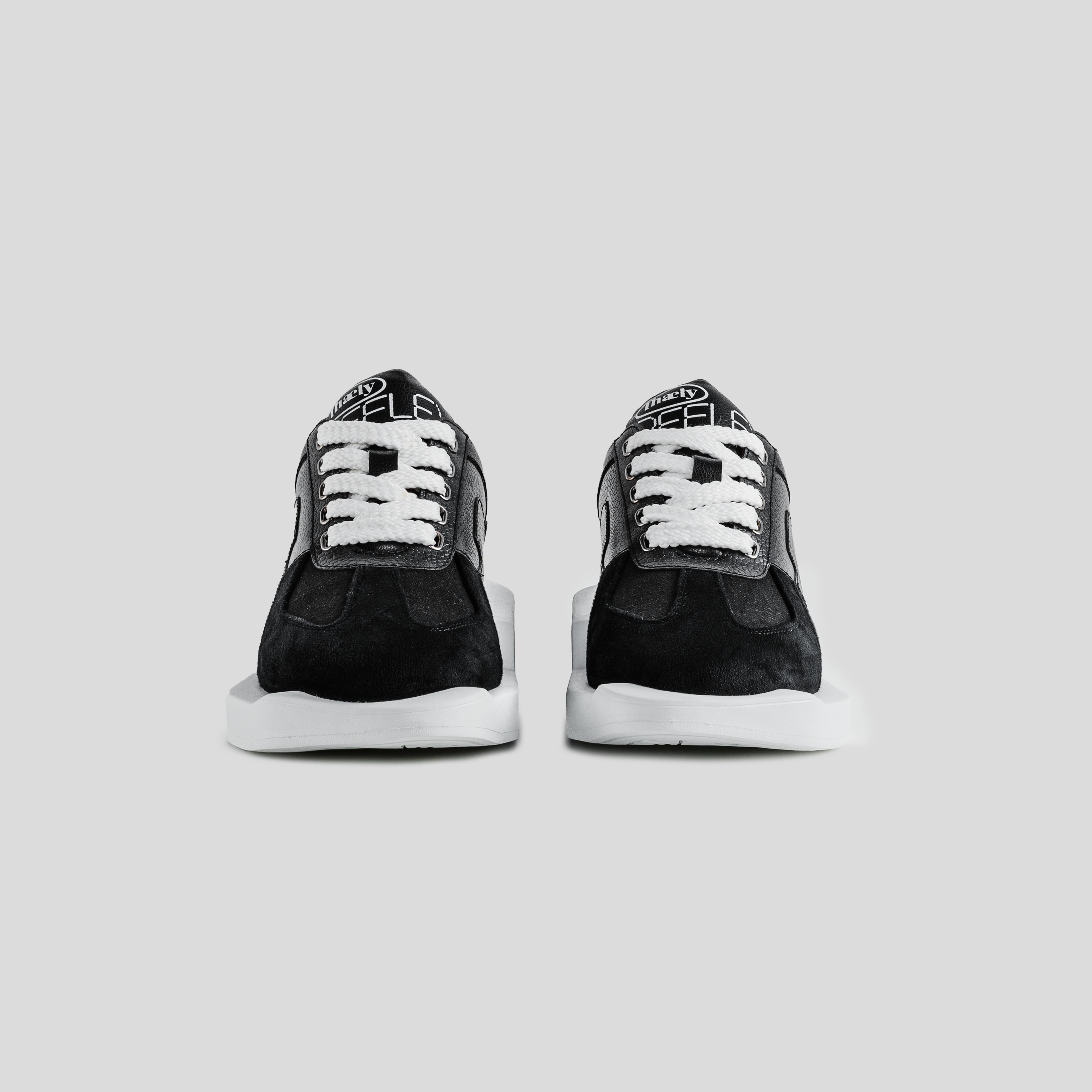 Black suede streetwear sneakers with white laces and thick soles on light gray background