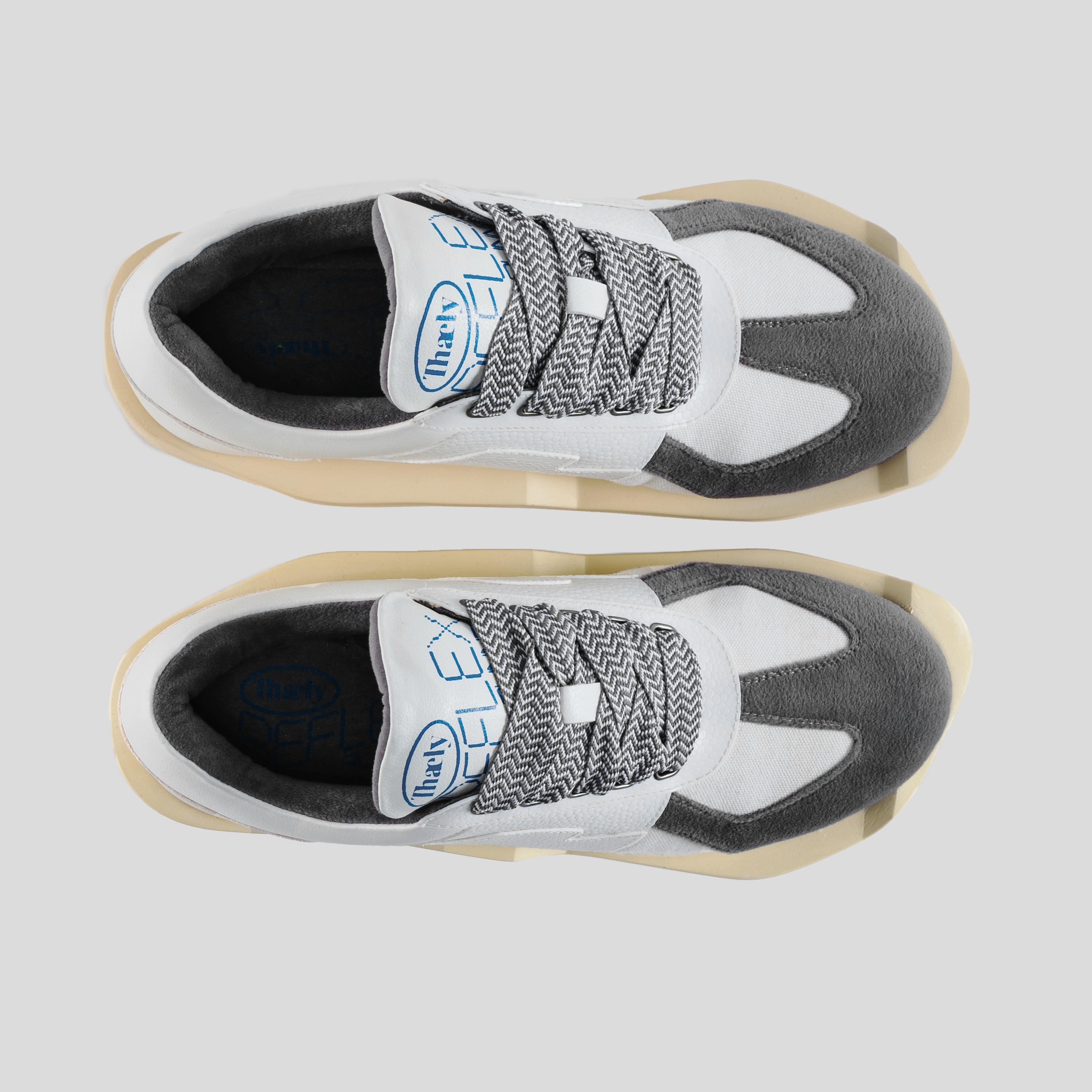 Top view of modern streetwear sneakers with white, grey, and black color blocking, thick patterned laces, and beige chunky soles.