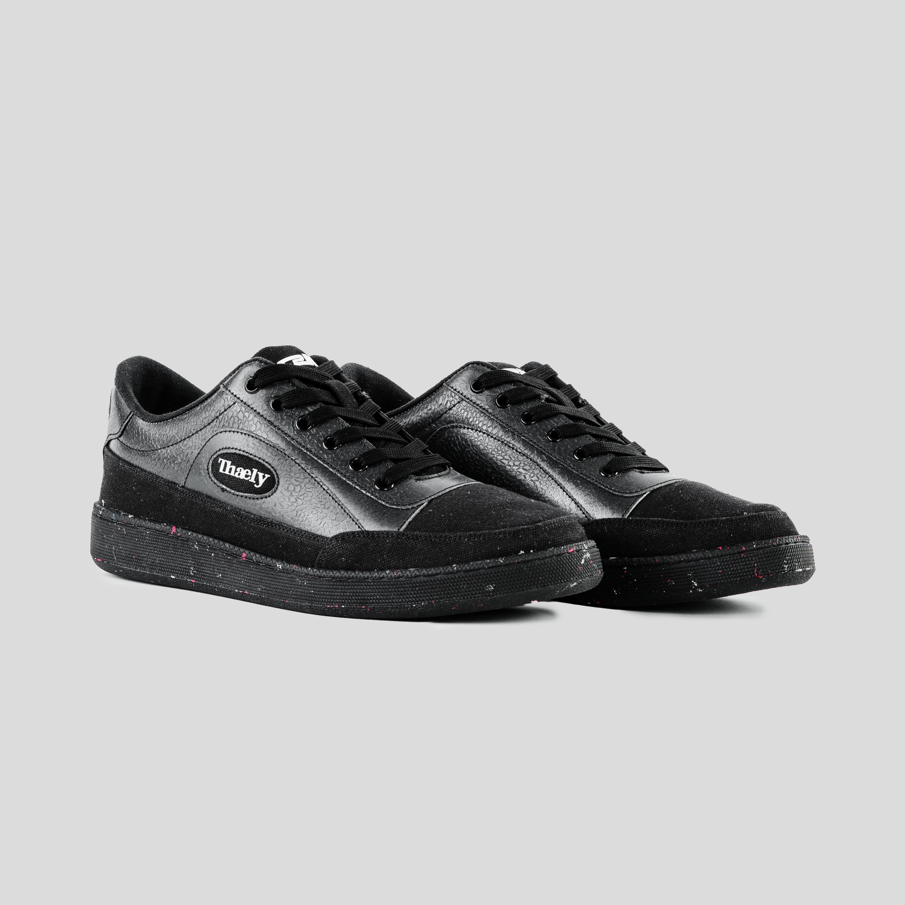 Black streetwear sneakers with suede and leather panels, speckled sole, and side logo patch