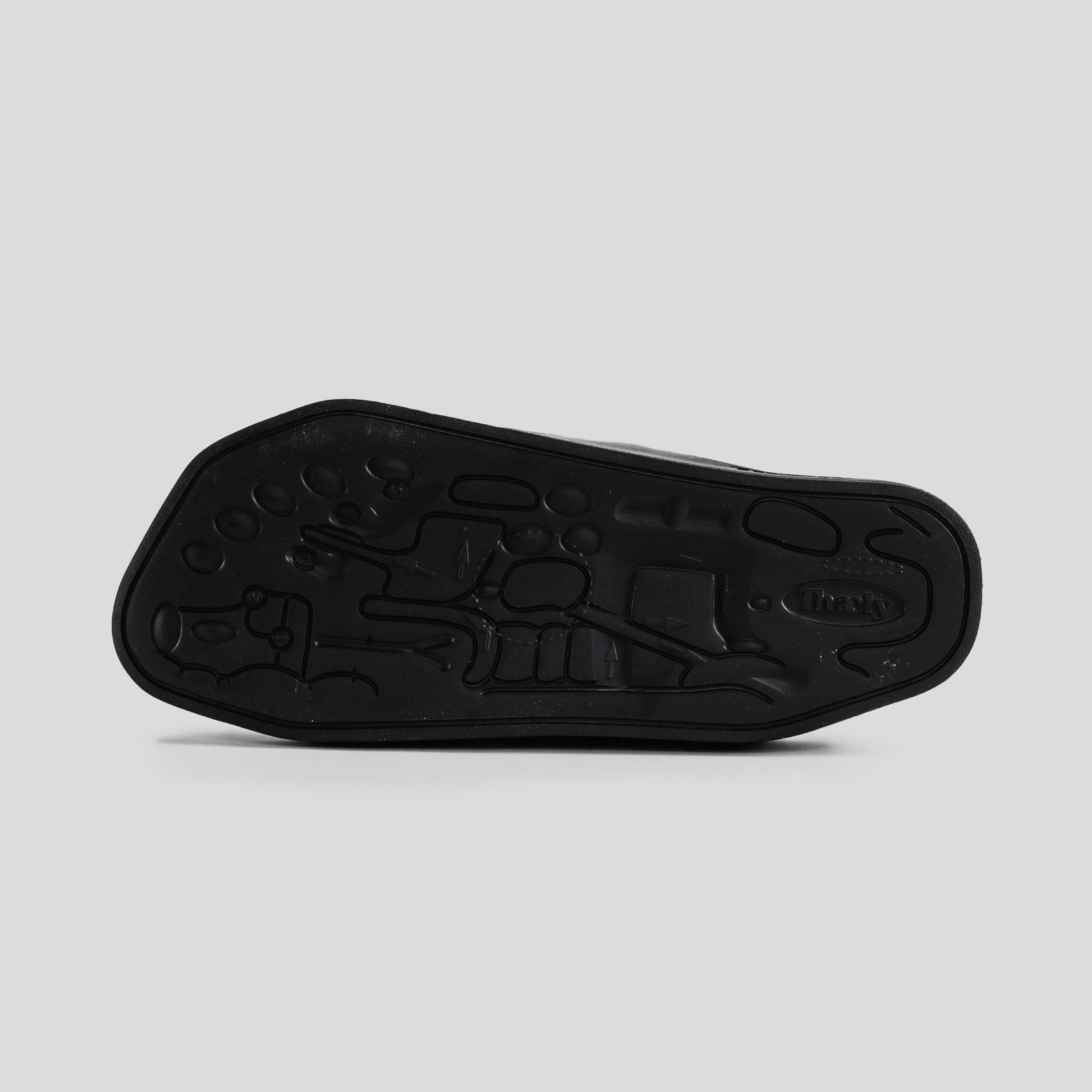 Black sneaker outsole with intricate tread pattern, photographed on light background