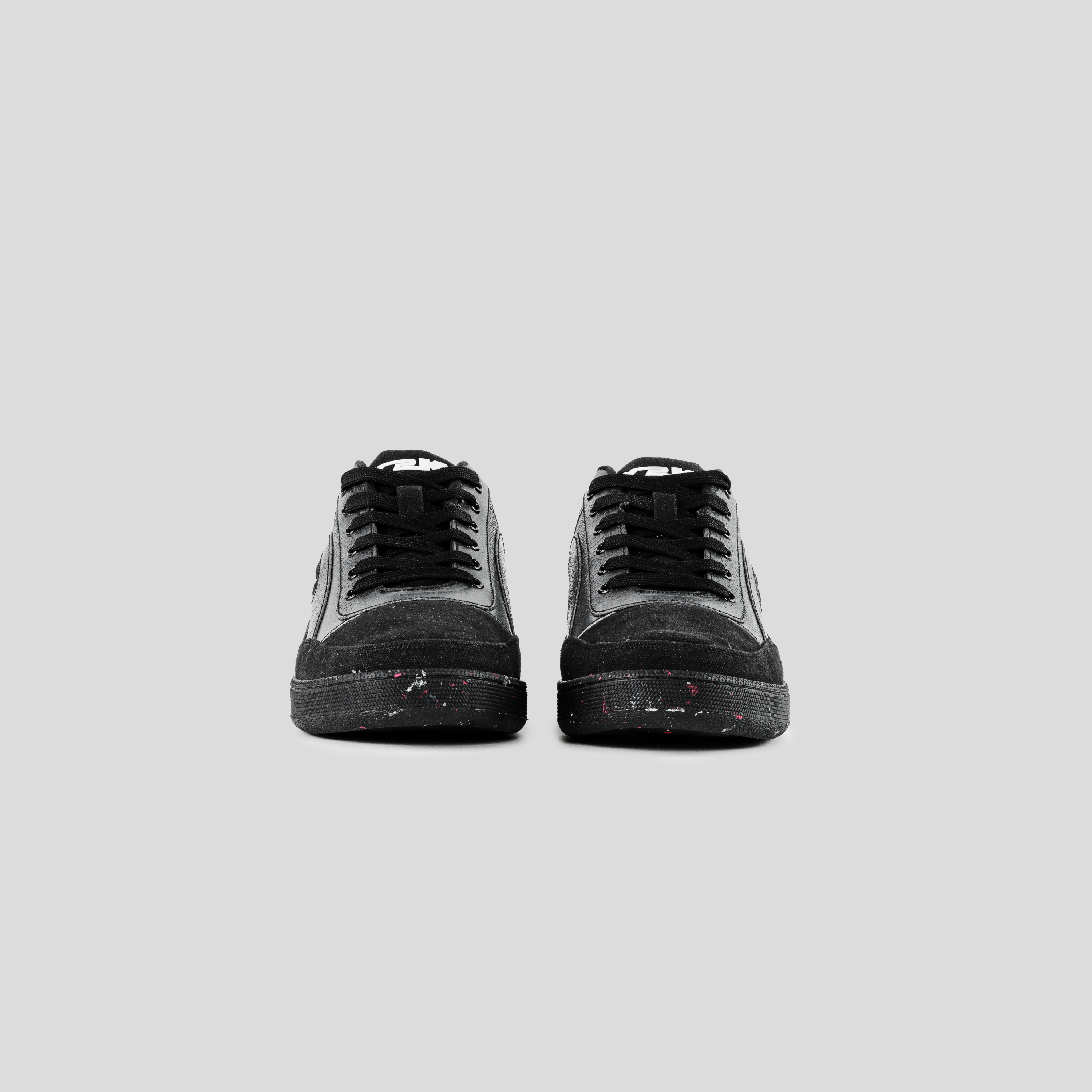 Black suede streetwear sneakers with paint splatter details, front view on gray background