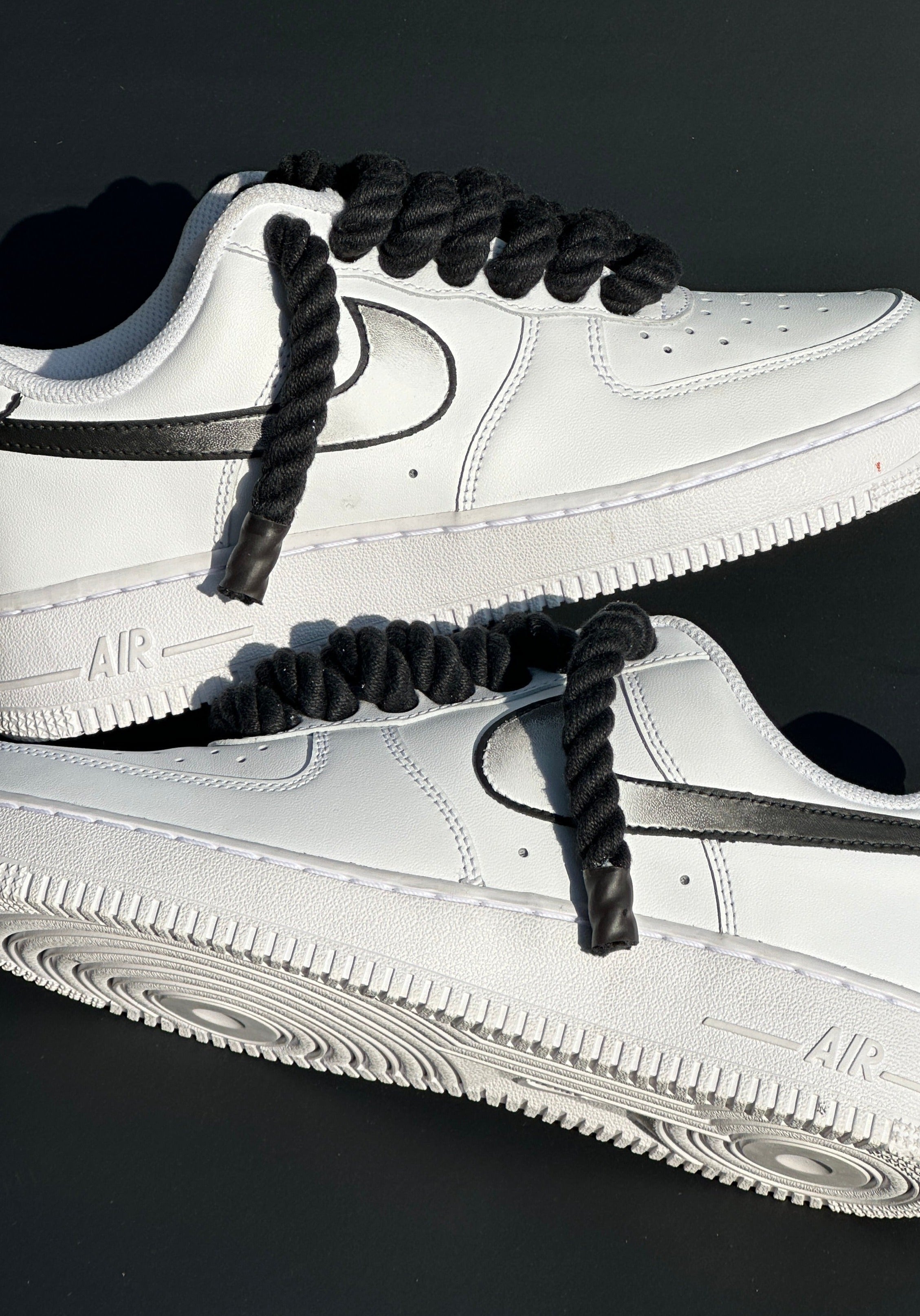 White leather low-top sneakers with black rope laces and black swoosh on dark background