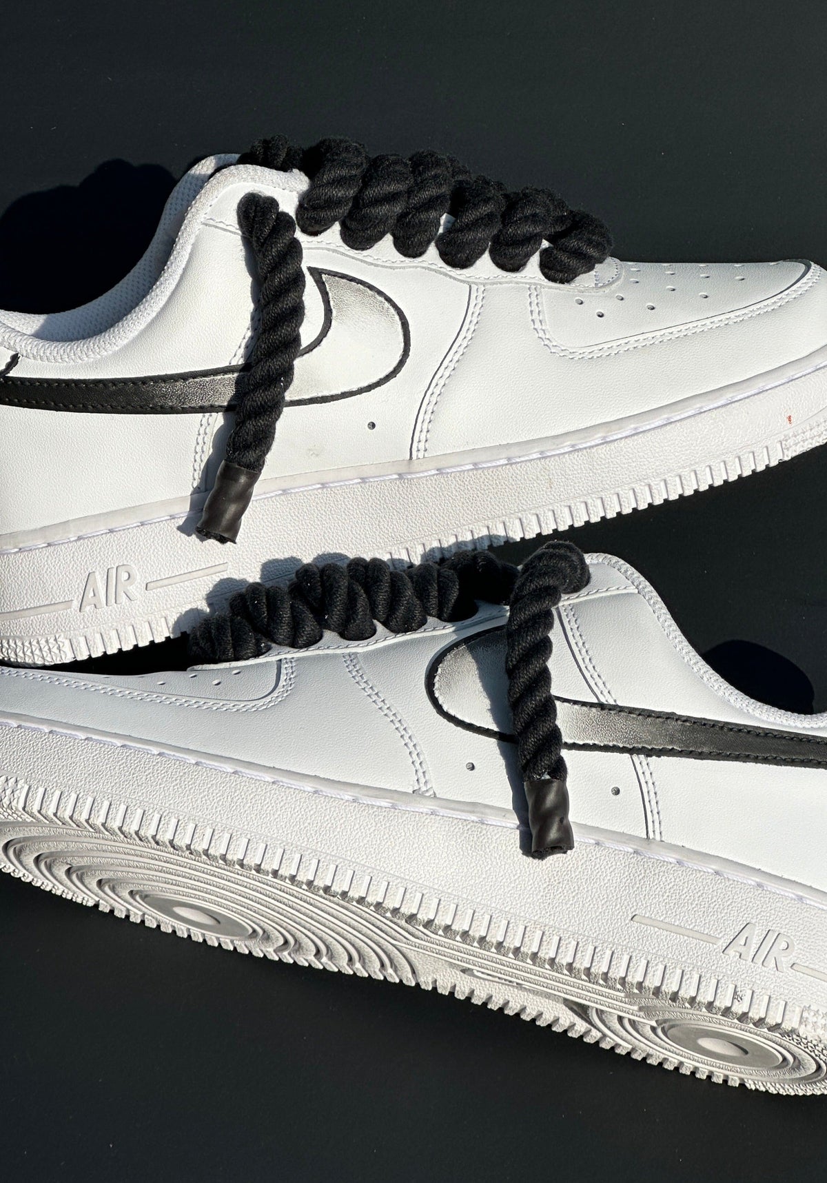 White leather low-top sneakers with black rope laces and black swoosh on dark background