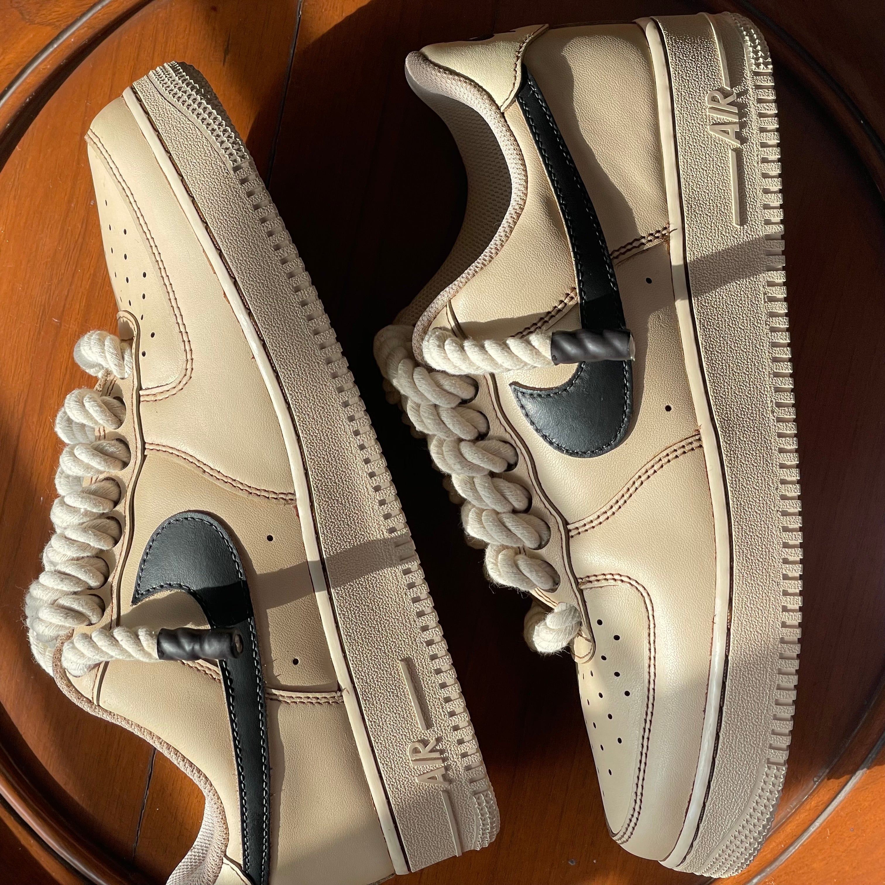 Tan and black leather sneakers with thick rope laces on a wooden surface, streetwear style