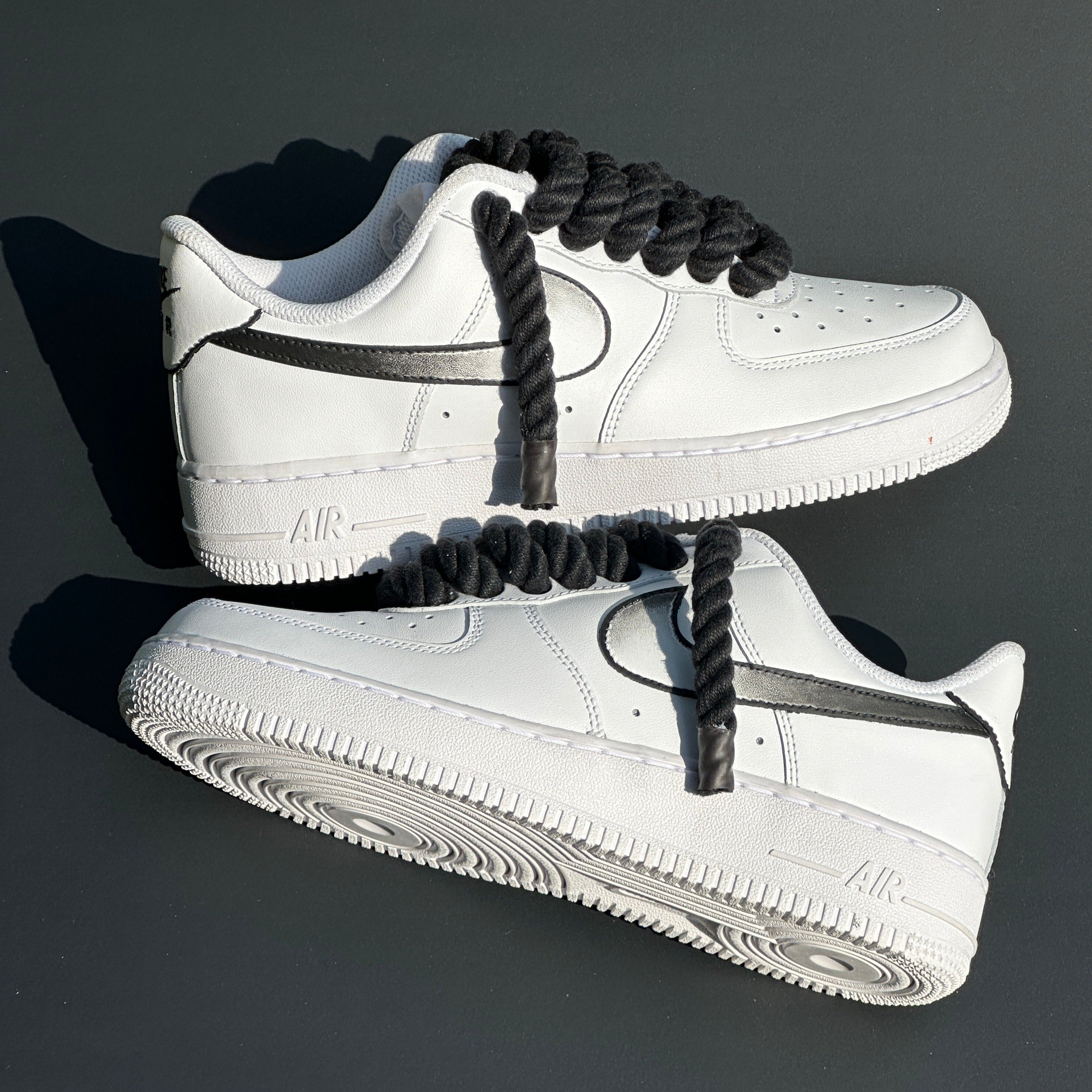 White streetwear sneakers with thick black rope laces and black swoosh detail on grey background
