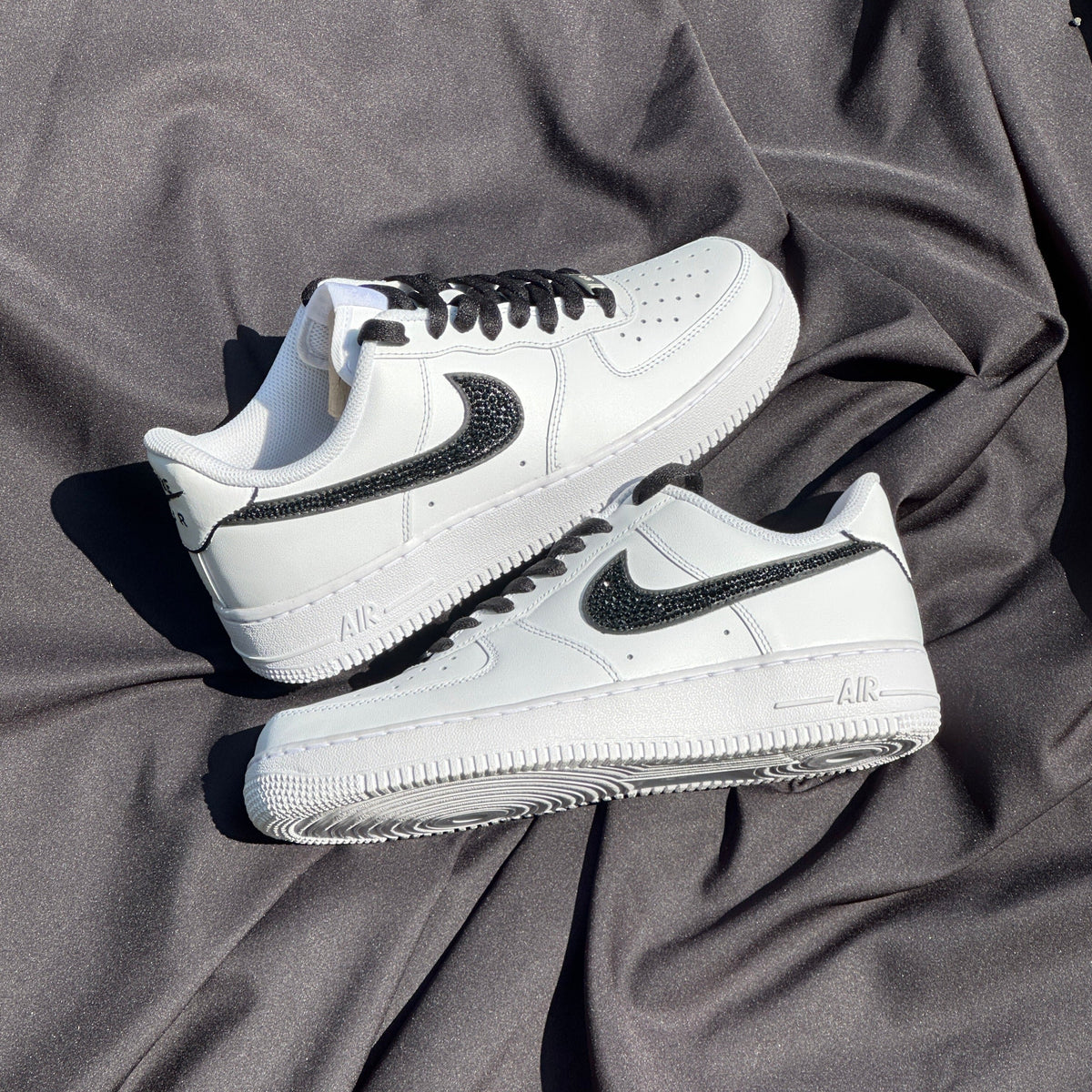 White Nike Air Force 1 sneakers with black textured swoosh and laces on gray fabric