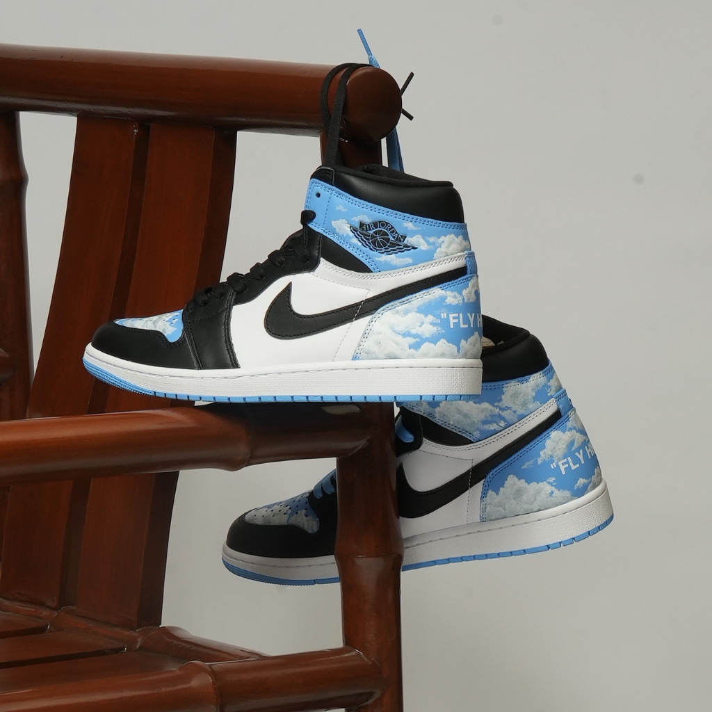 Blue and white high-top sneakers with black swoosh, cloud pattern, displayed on wooden chair.
