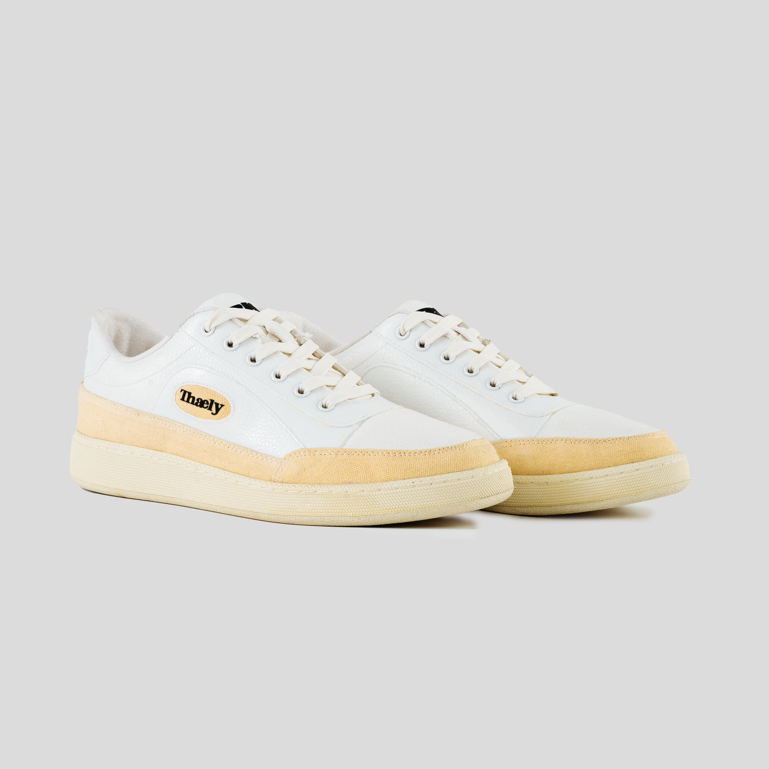 White and beige low-top streetwear sneakers with logo patch, neutral background