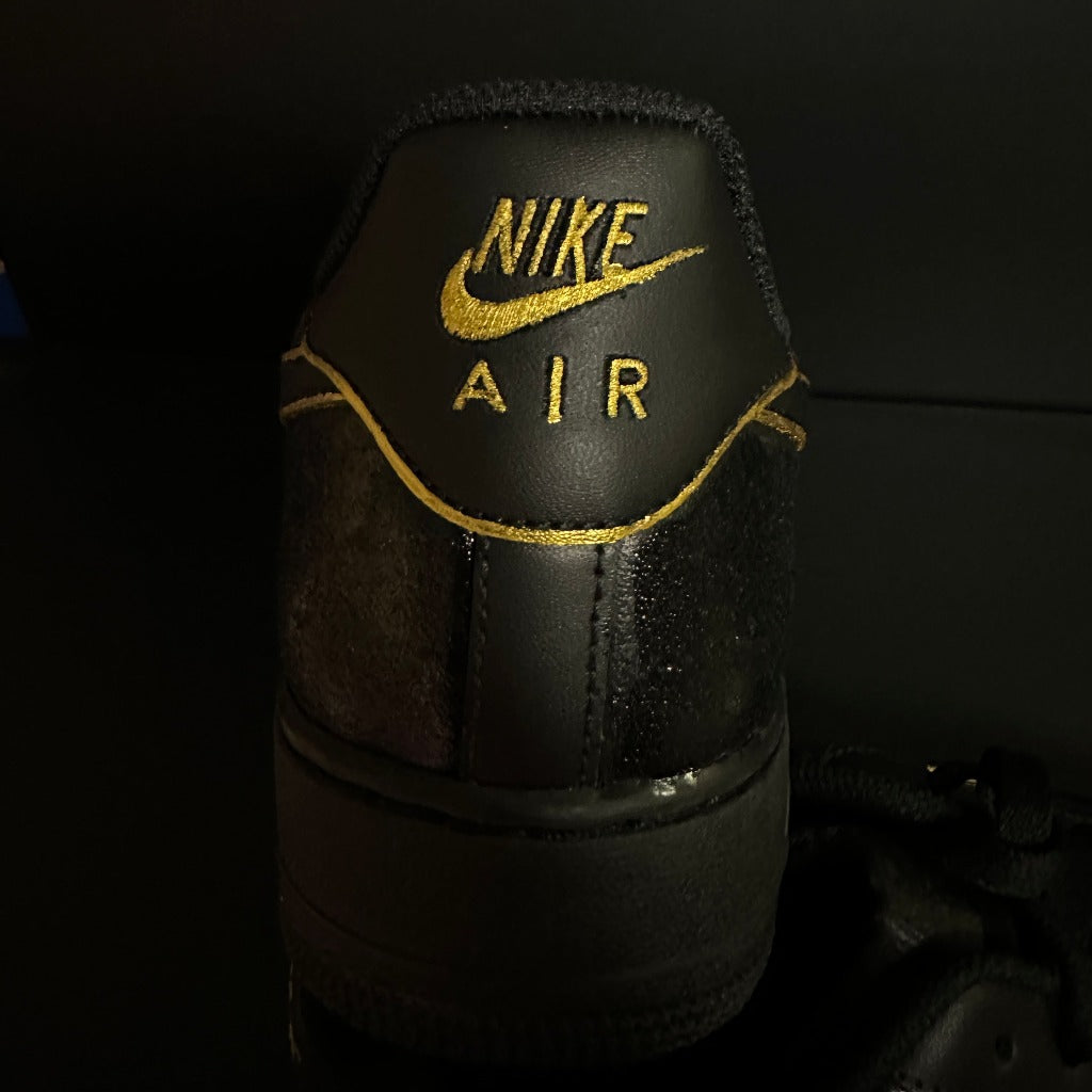 Black Nike Air sneaker with gold embroidered logo and stitching, rear view