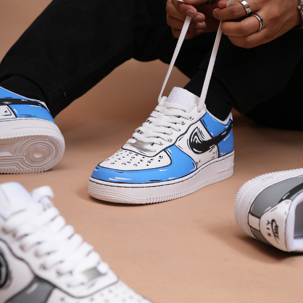 Person tying laces on blue and white cartoon-style designer sneakers with bold black accents