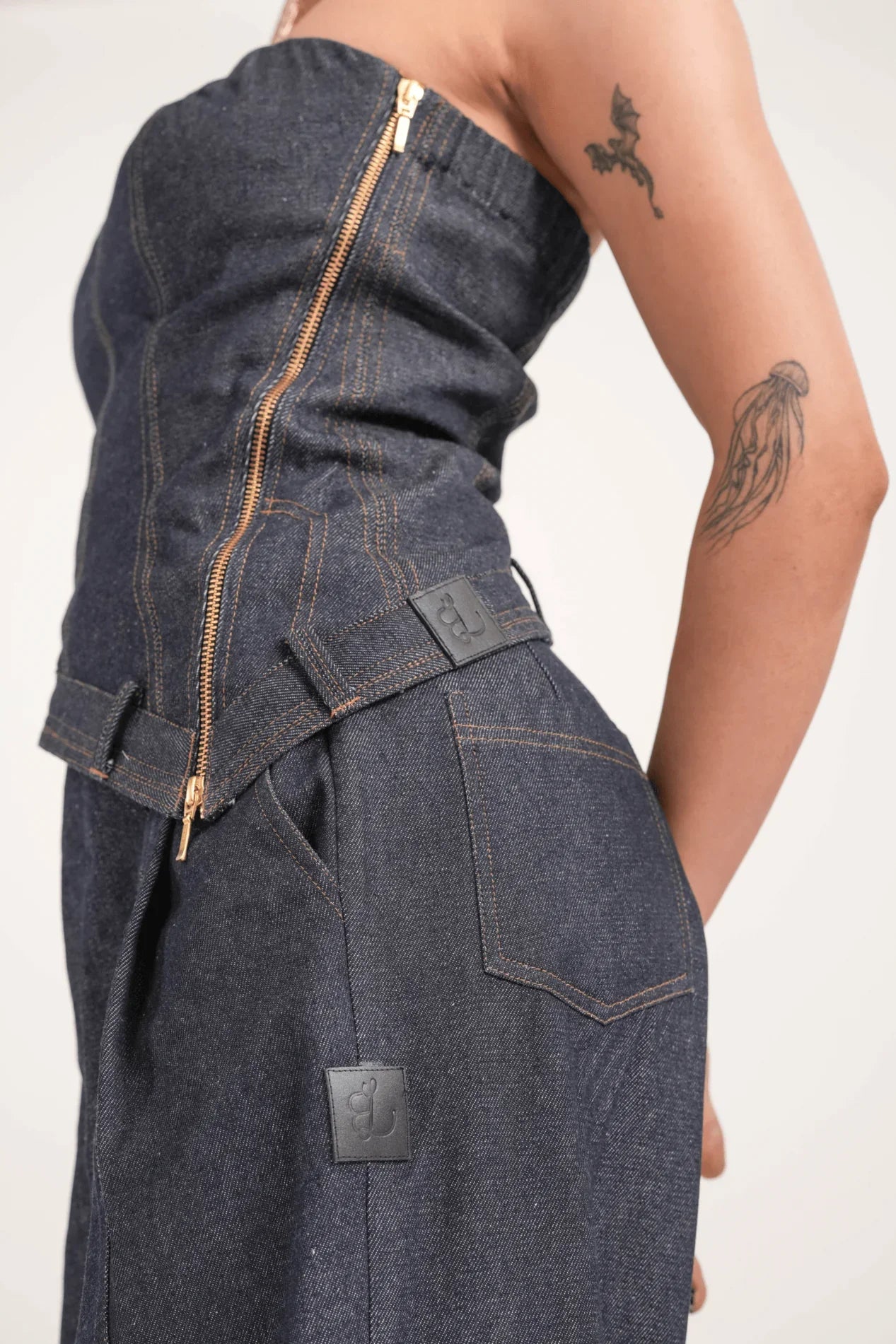 Close-up of woman wearing dark blue denim outfit with zipper and brown stitching, jellyfish and dragon tattoos on arm