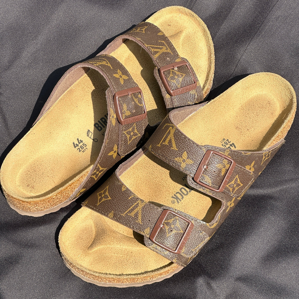 Brown luxury print buckle sandals with cork soles on a black fabric background