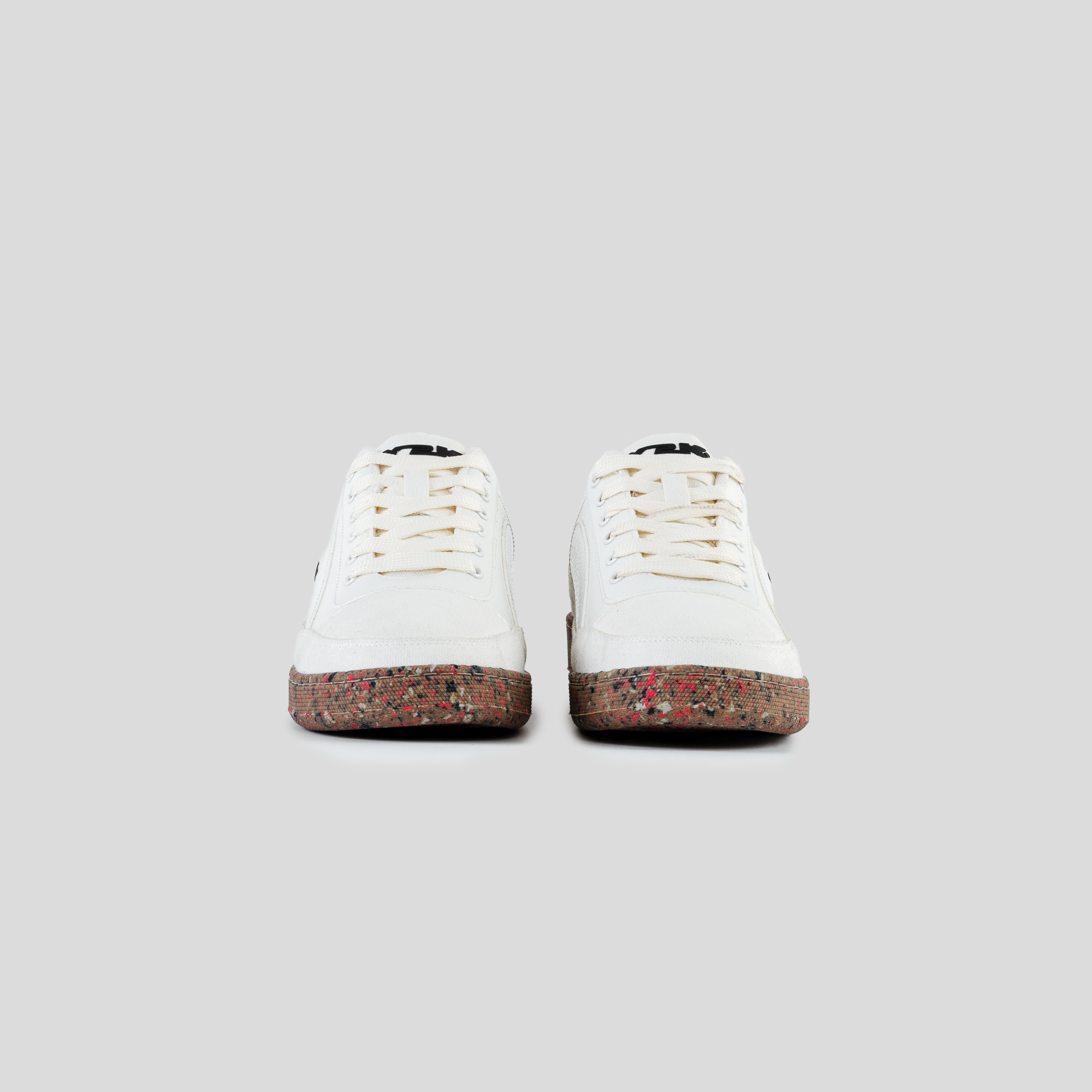 White streetwear sneakers with speckled gum soles, viewed from the front on a plain background