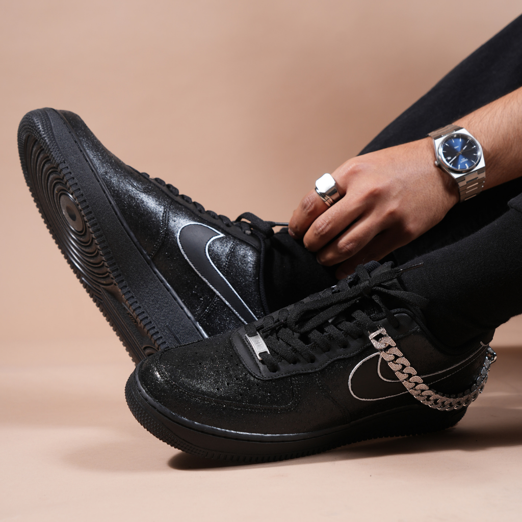 Black streetwear sneakers with silver details and chain accessory on foot, worn with jewelry.