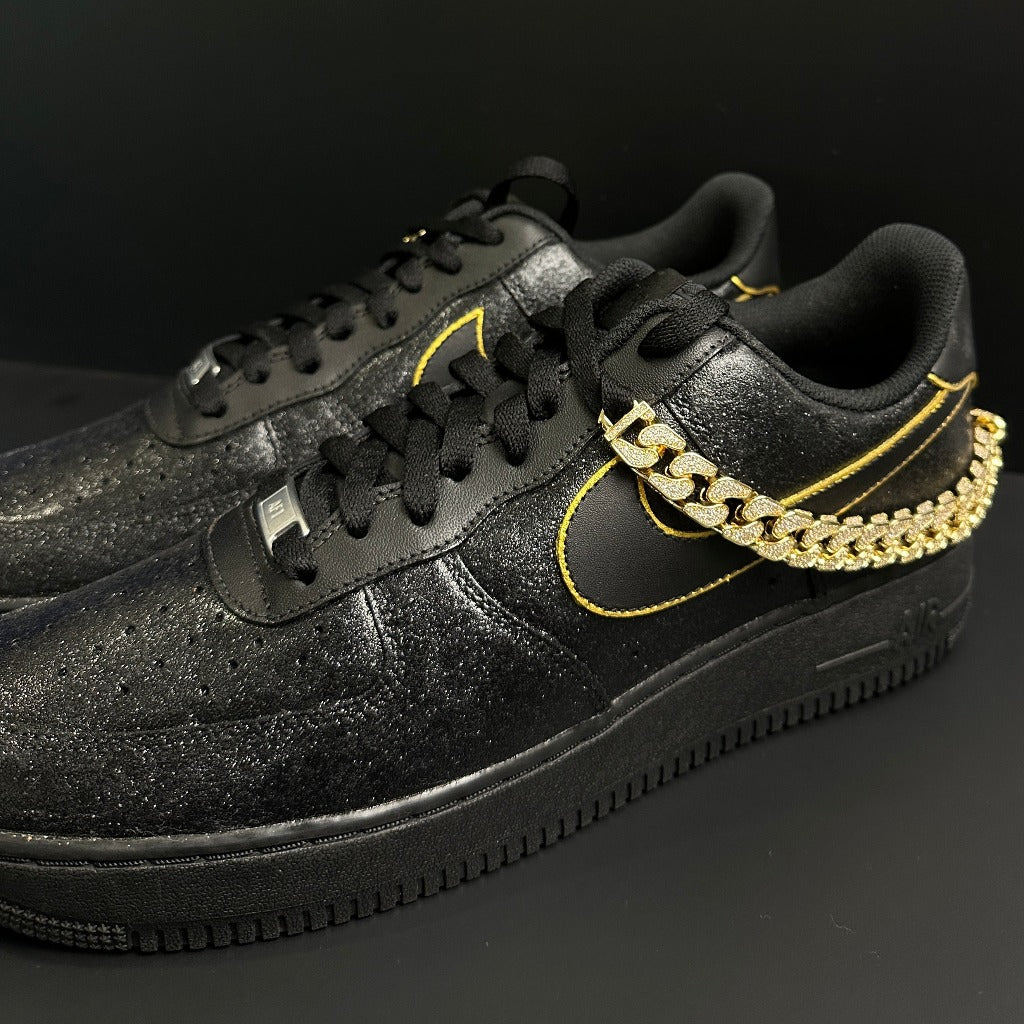 Black streetwear sneakers with gold chain detail, yellow trim, and glitter accents