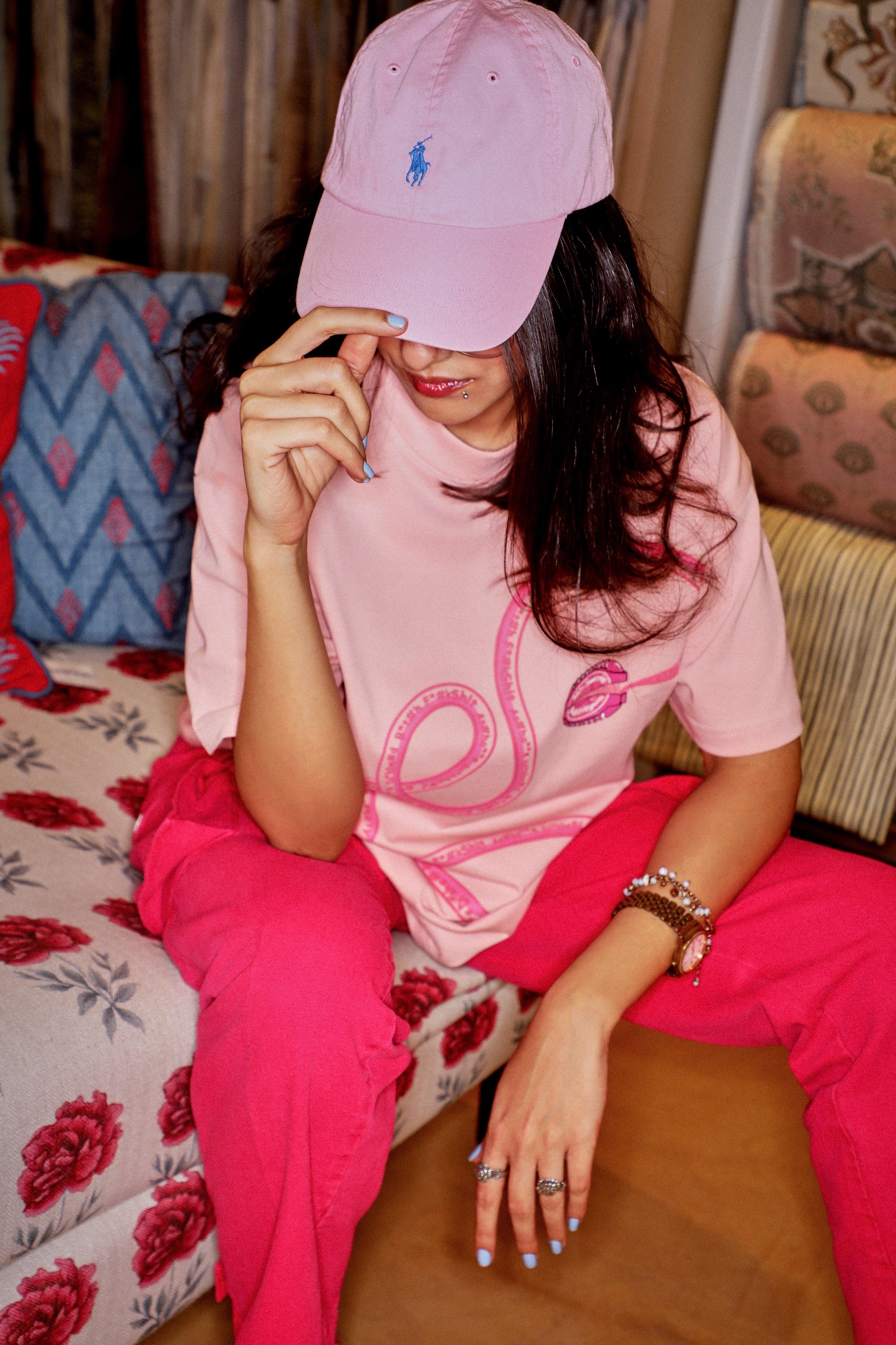 Woman in pink streetwear outfit with pink cap and graphic t-shirt sitting on floral sofa