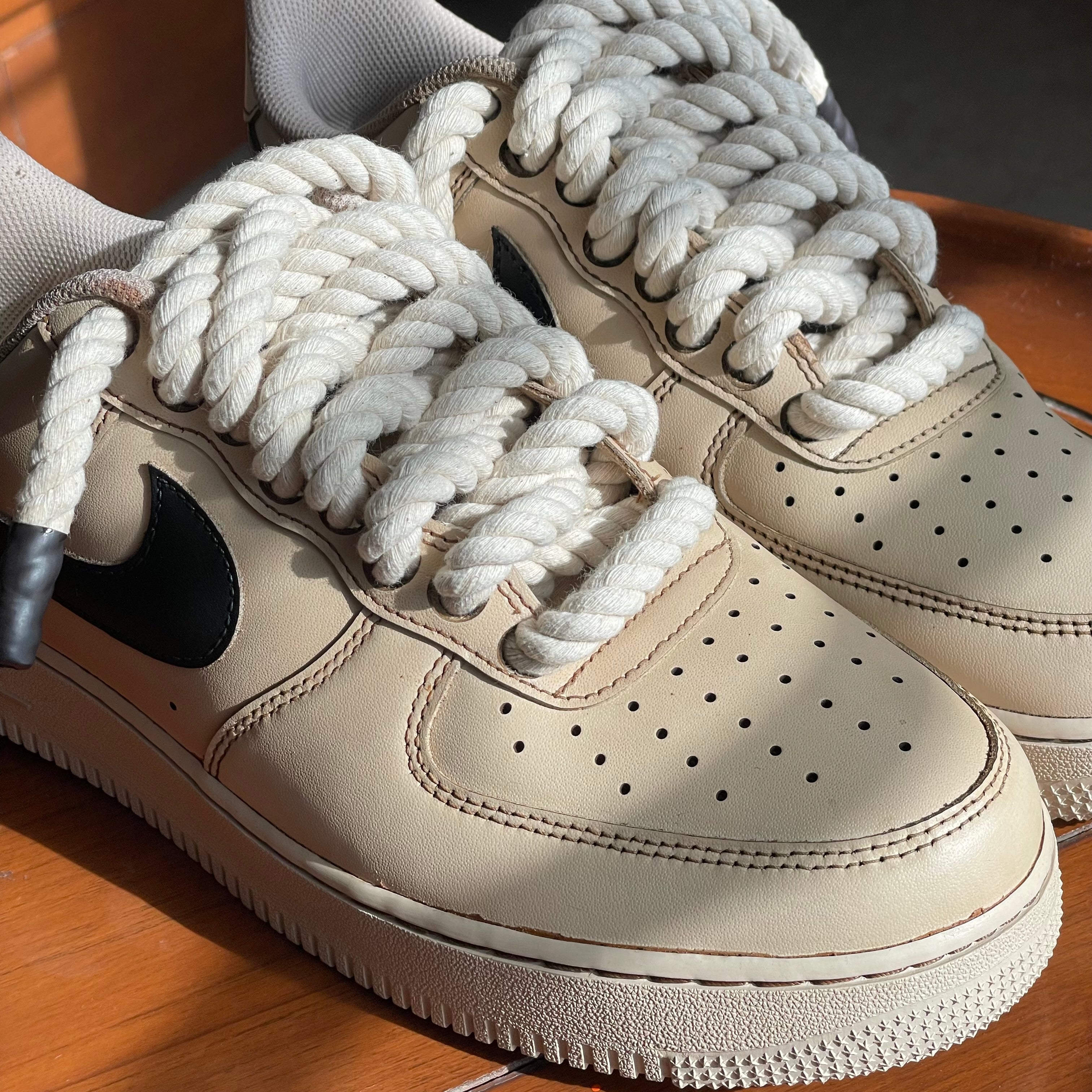 Beige leather sneakers with oversized rope laces and black swoosh logo, streetwear style
