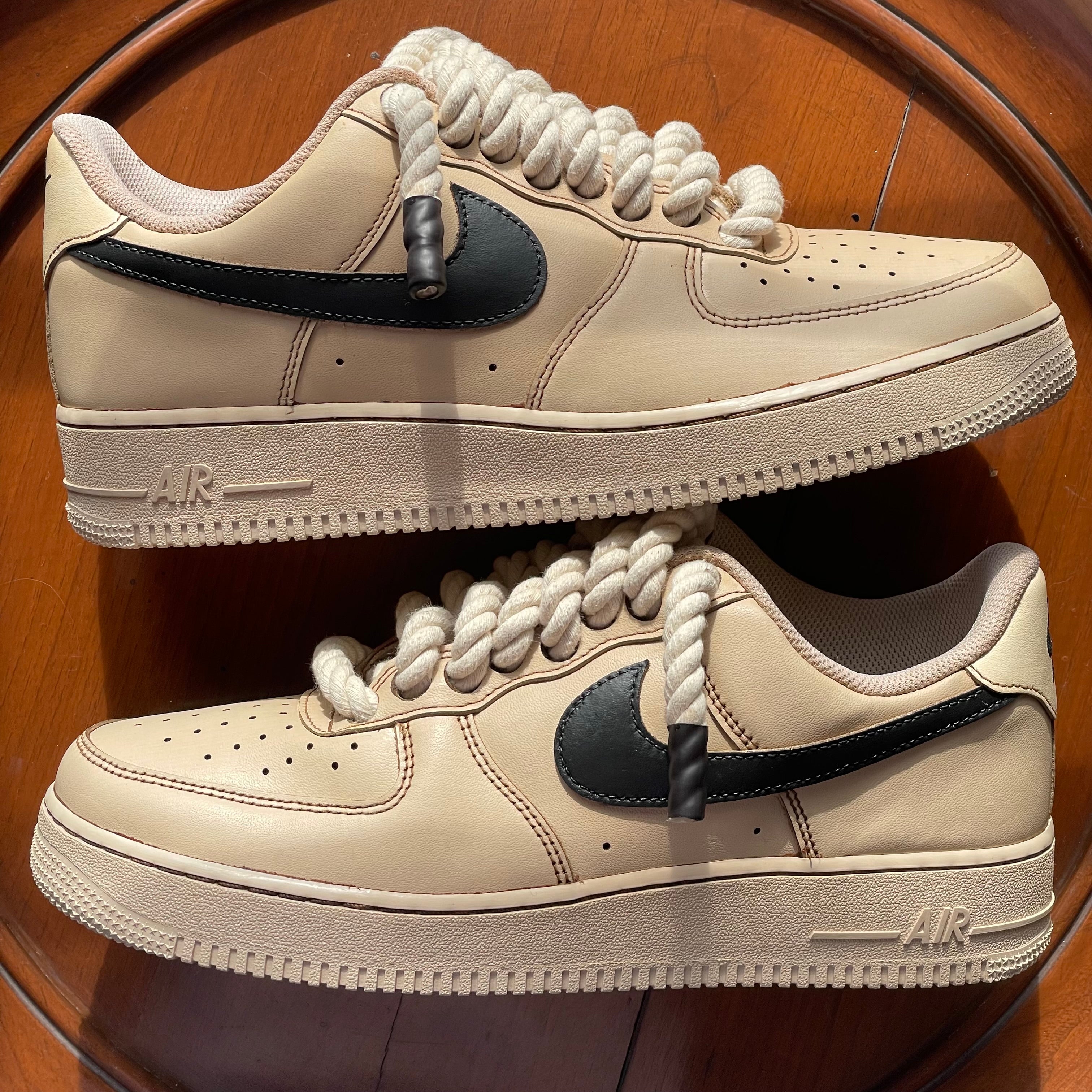 Beige streetwear sneakers with thick rope laces and black swoosh on wooden surface
