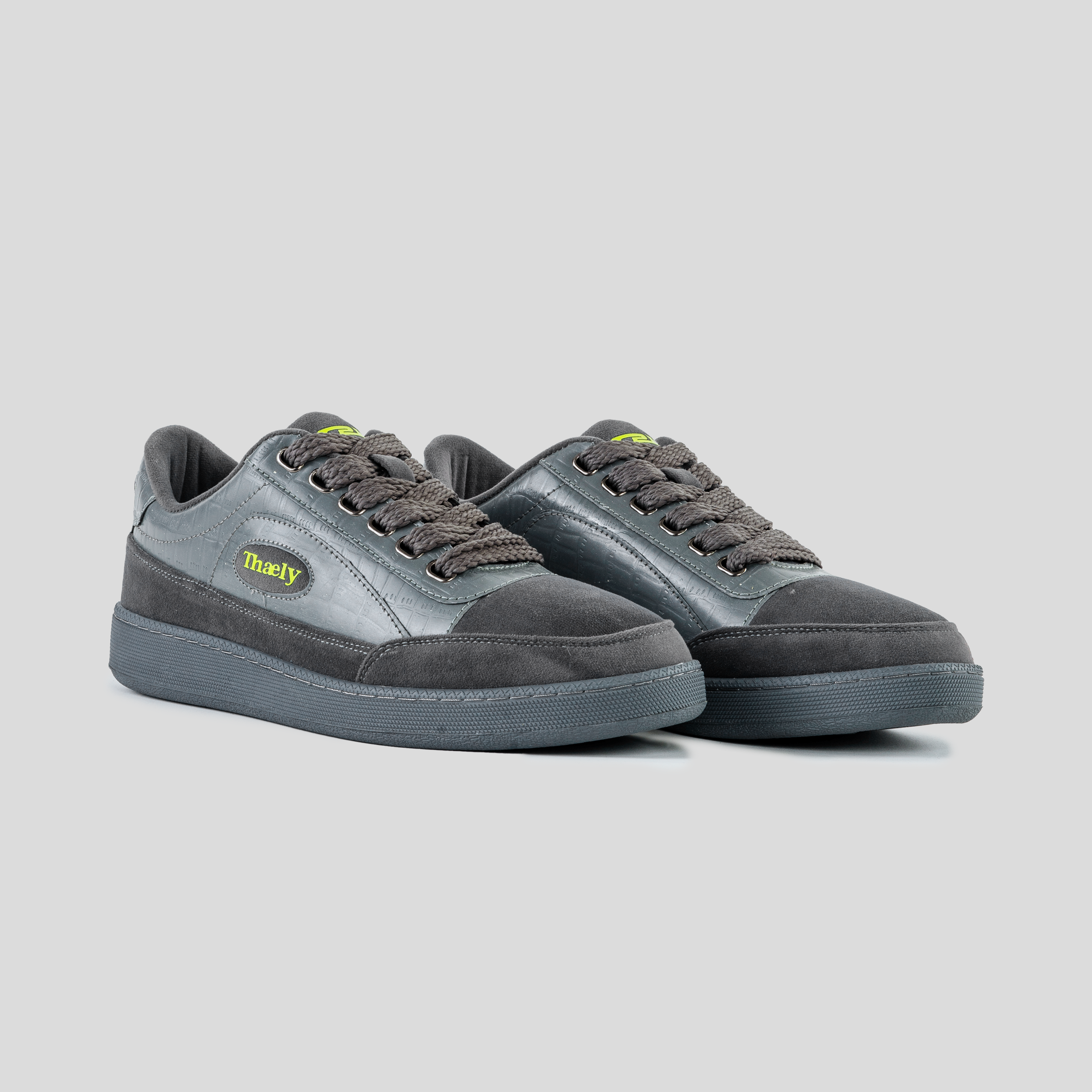 Dark grey low-top streetwear sneakers with textured panels and thick laces on a light background