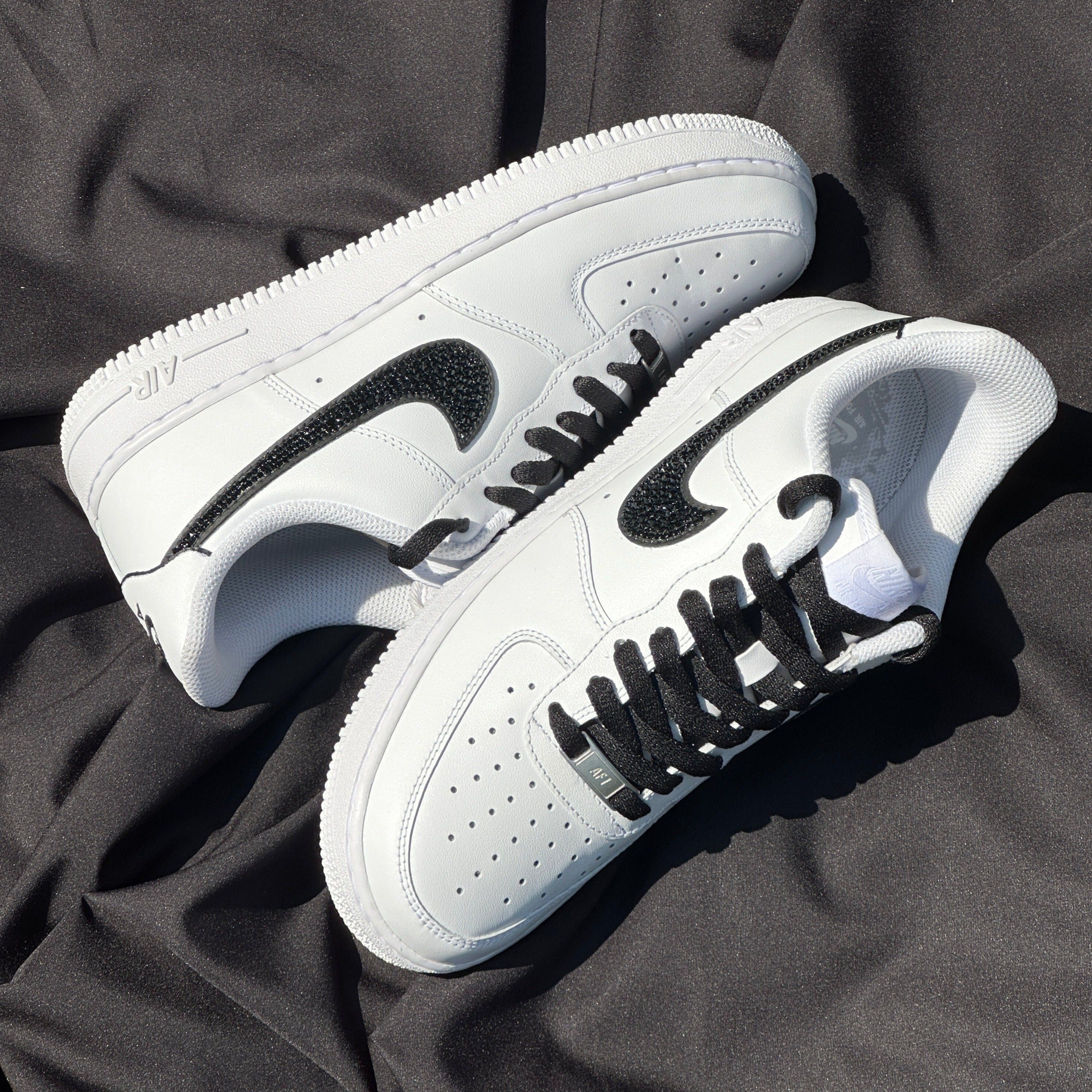 White and black Nike Air Force 1 sneakers with black laces on a black fabric background