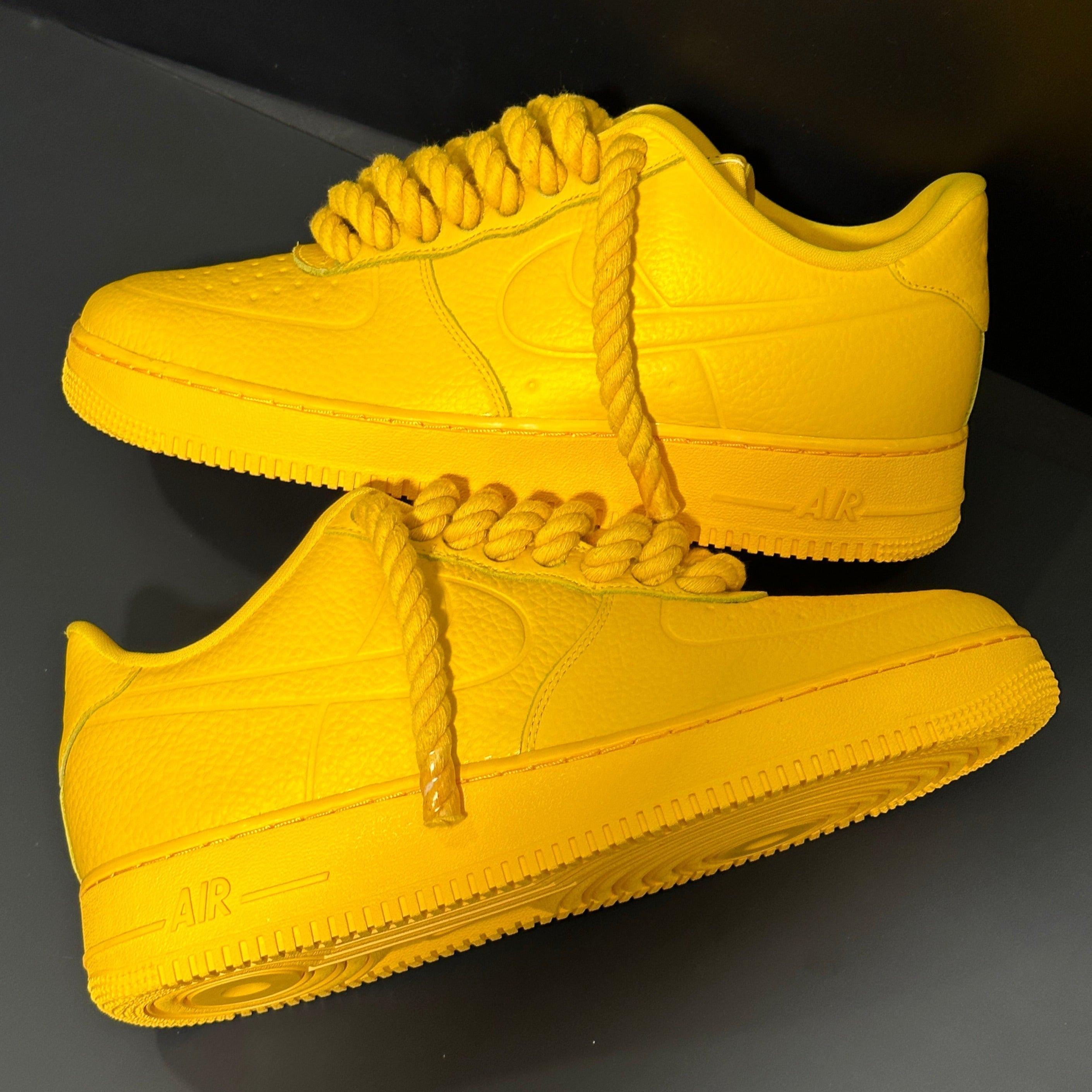 Bright yellow low-top sneakers with chunky rope laces on a dark background
