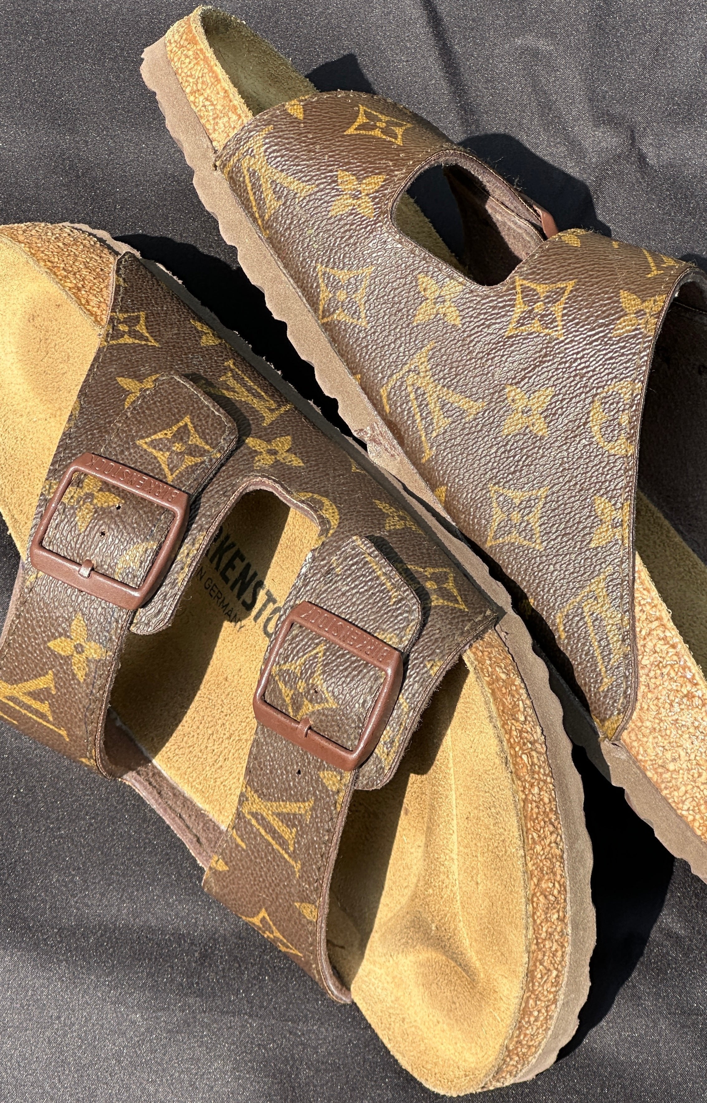 Brown designer slide sandals with gold monogram pattern and cork footbed on black background