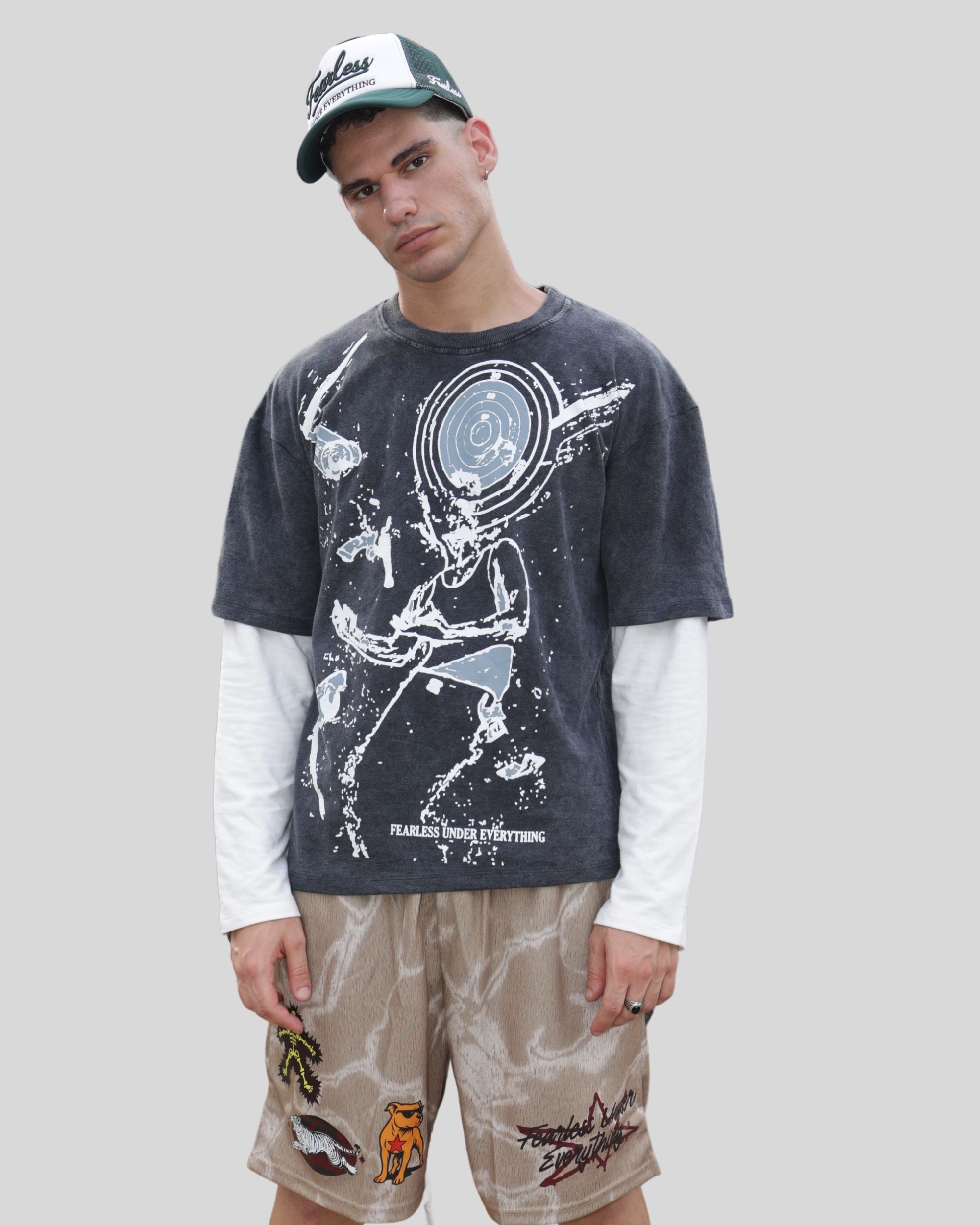 Man wearing Fearless Under Everything Mad-Max Shorts and graphic t-shirt posing against grey background.