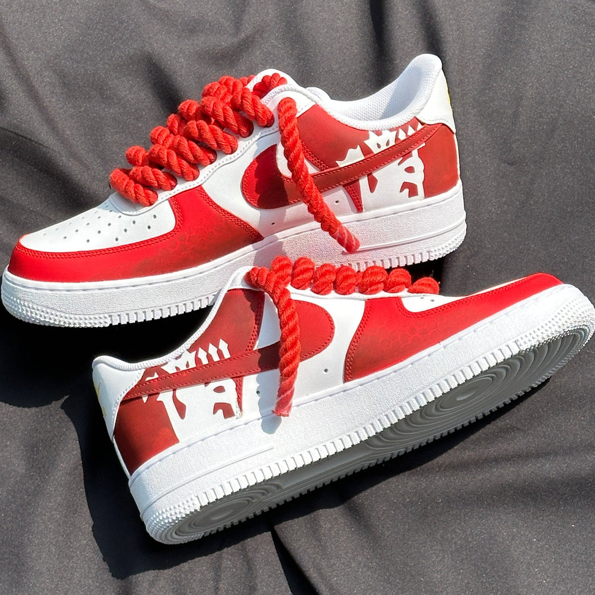 Red and white low-top streetwear sneakers with thick red laces on dark fabric background