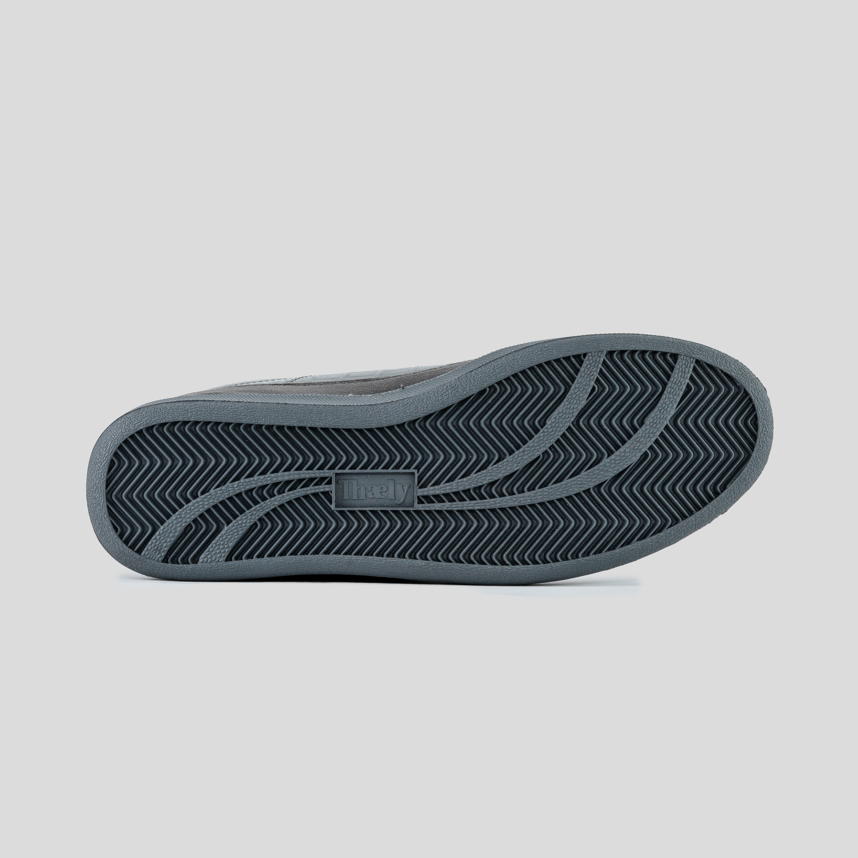 Close-up of a sneaker outsole with herringbone traction pattern on a grey background.