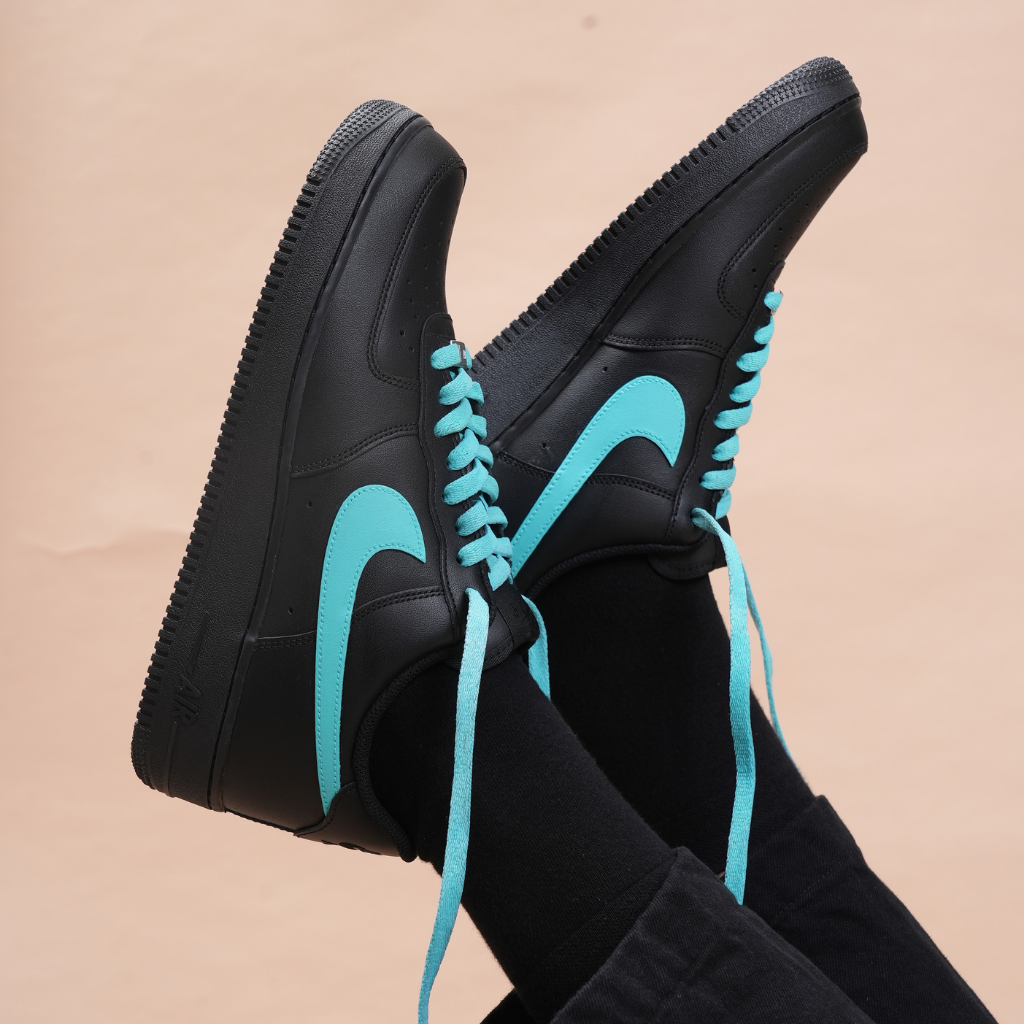 Black streetwear sneakers with turquoise swoosh and laces, worn with black pants