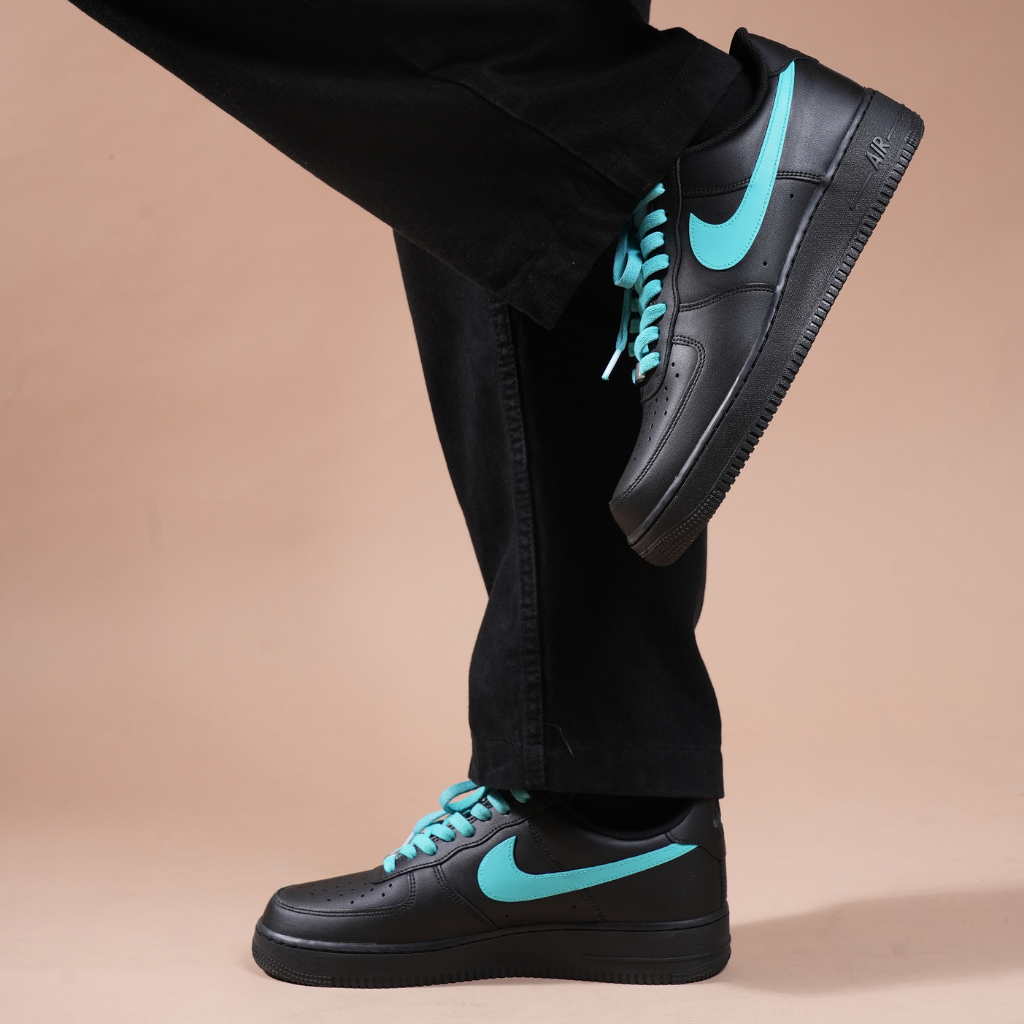 Black low-top sneakers with teal swoosh and laces, streetwear fashion on beige background