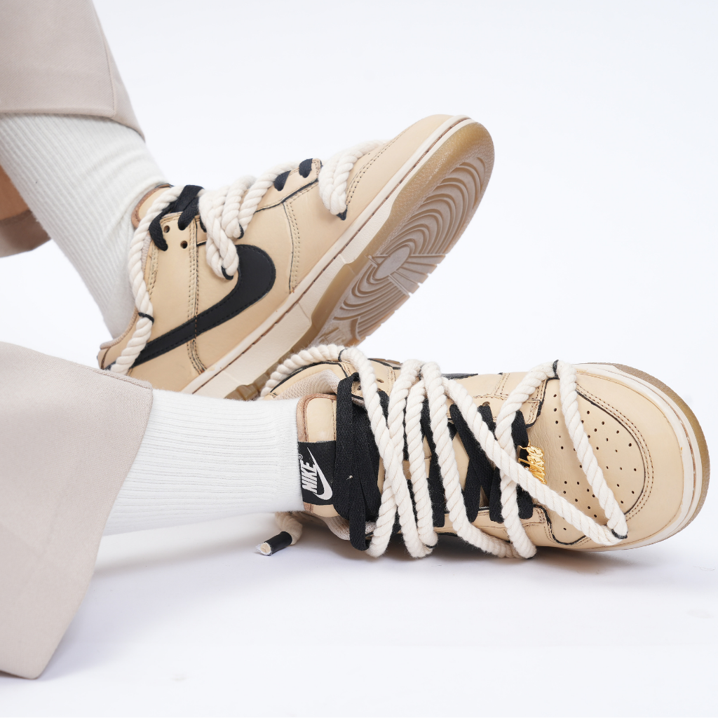 Beige and black Nike Dunk sneakers with thick rope laces worn with white socks