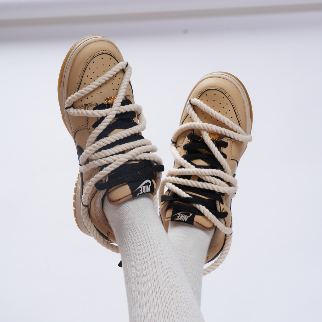 Tan and black Nike sneakers with thick rope laces, worn with white crew socks.
