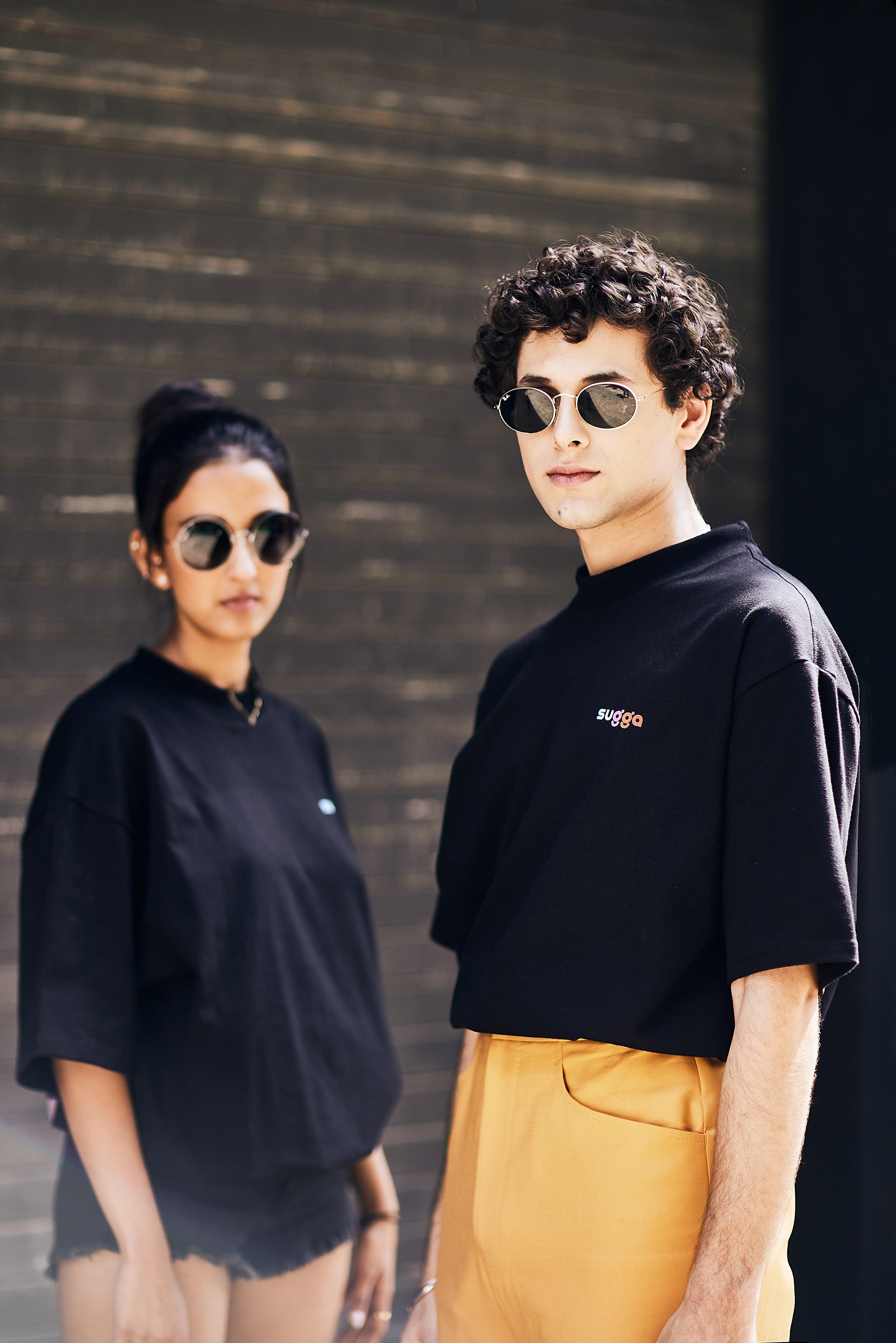 Two people in streetwear, wearing black oversized t-shirts and sunglasses, urban background