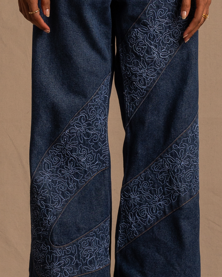Dark wash denim jeans with intricate blue embroidered patterns and relaxed streetwear fit