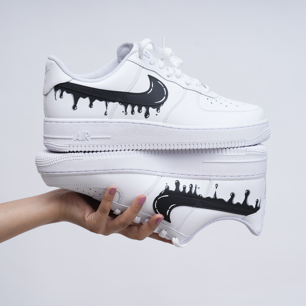 White custom streetwear sneakers with black dripping Swoosh logo held in hand, clean background