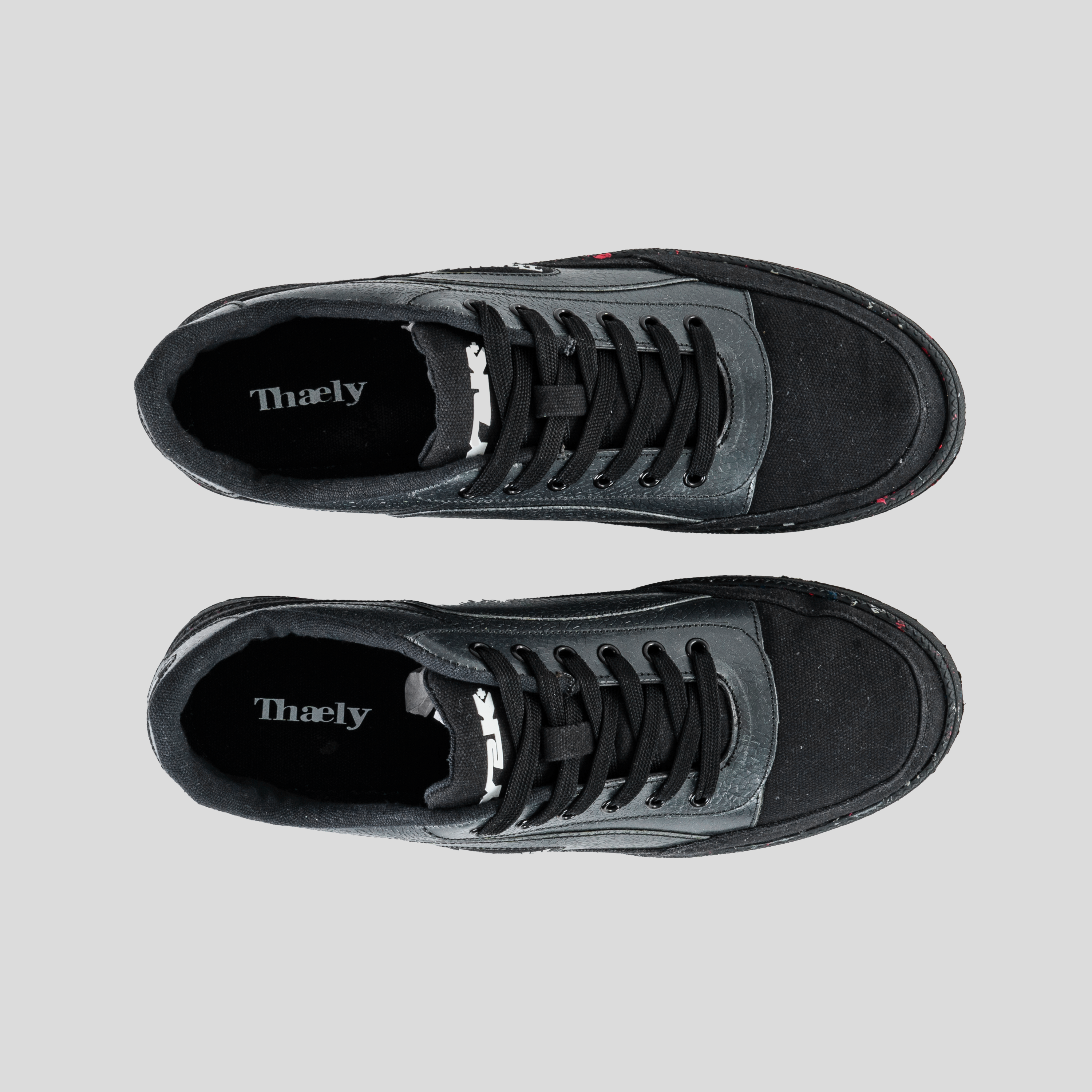 Top view of black Thaely low-top sneakers with black laces on a light background.