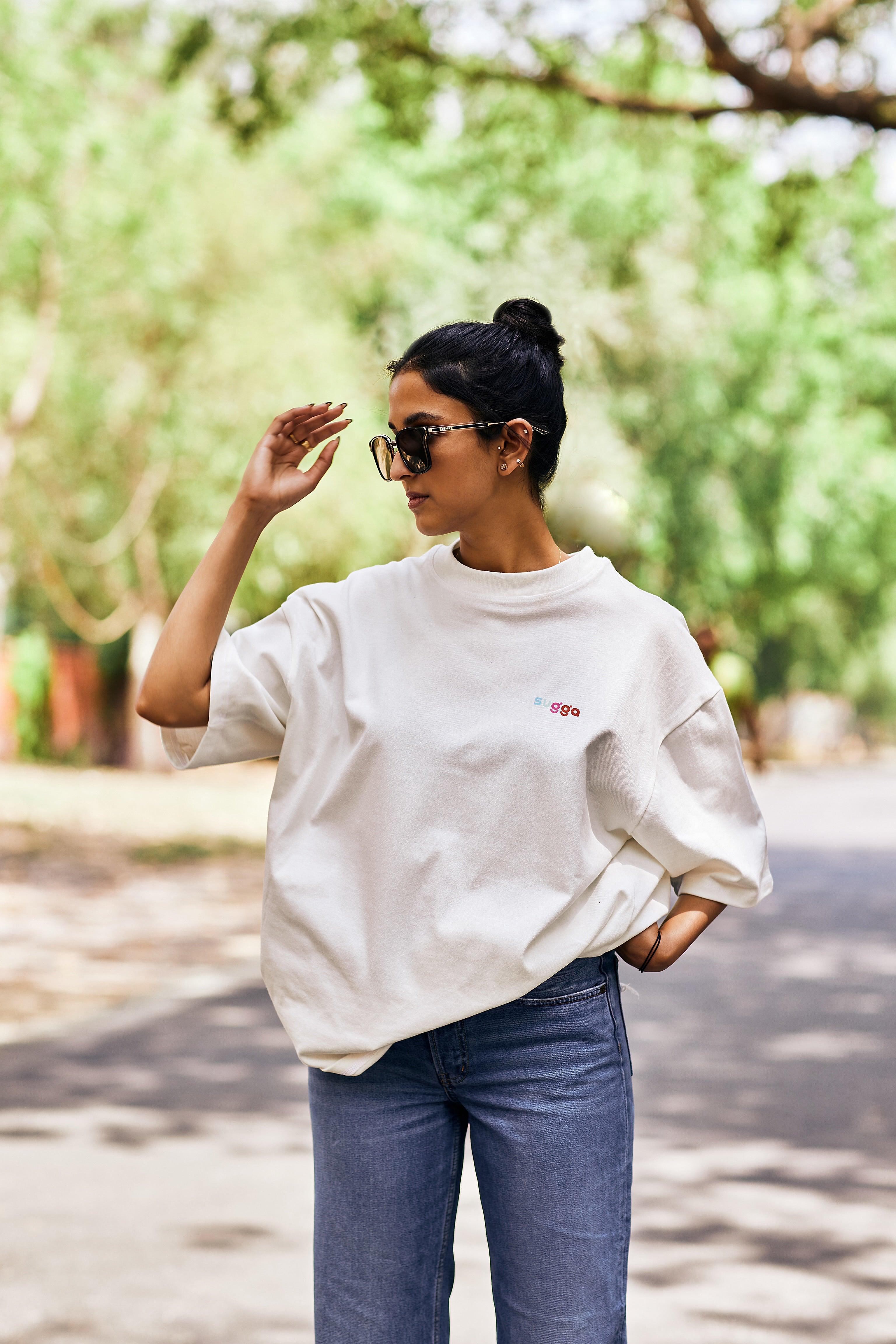 Woman in streetwear style with oversized white graphic t-shirt, jeans, and sunglasses outdoors
