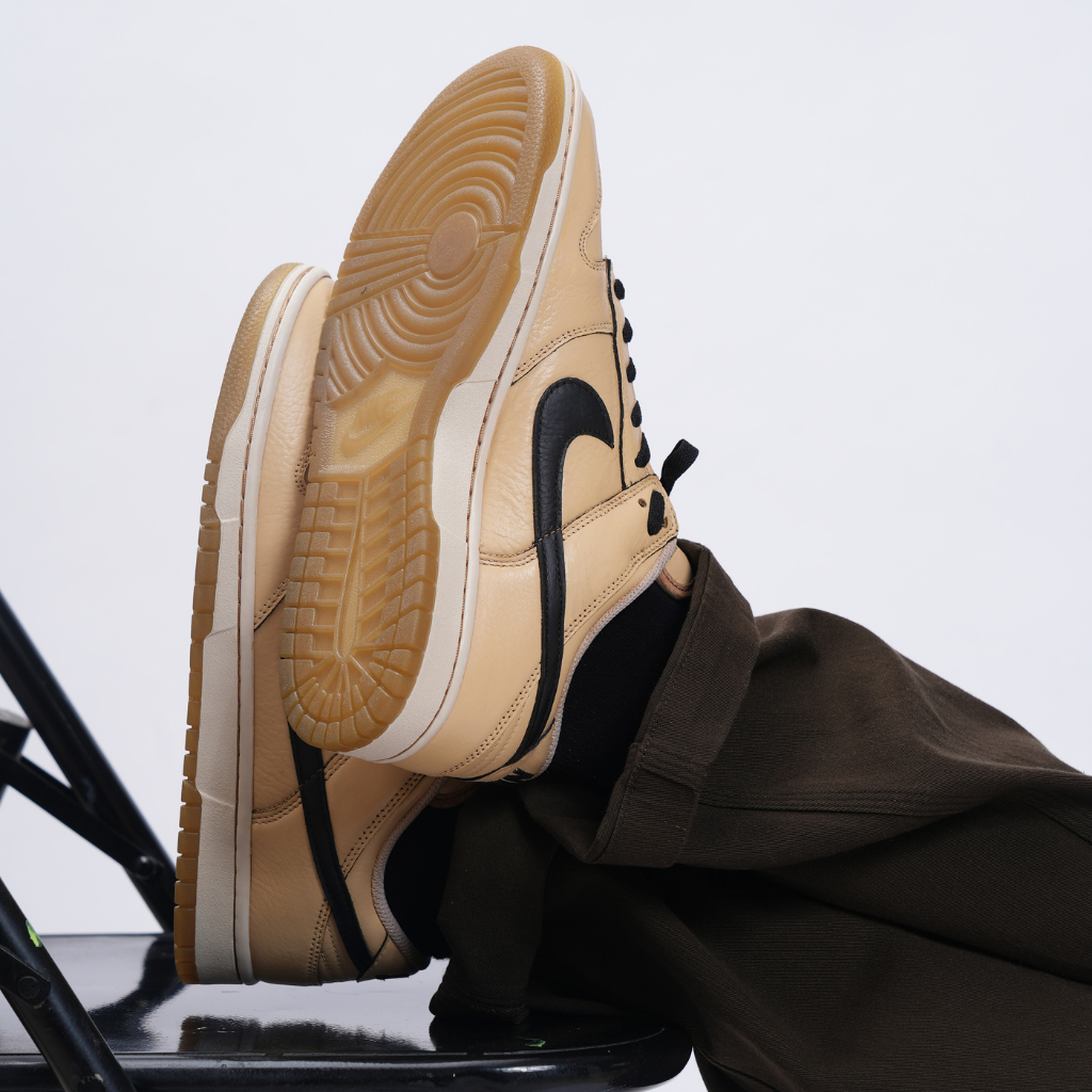 Tan and black low-top sneakers with gum soles styled with brown pants on a chair, streetwear fashion